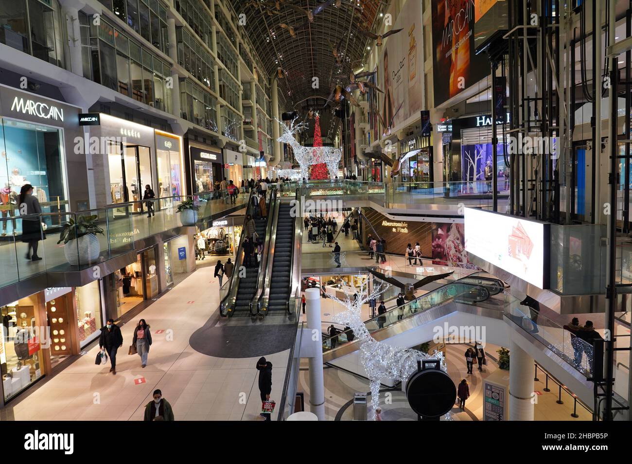 Das Eaton Centre in Toronto ist ein mehrstufiger Einkaufszentrum mit hellen Weihnachtsdekorationen und Einkaufsküppern, die aufgrund der Pandemie Gesichtsmasken tragen Stockfoto