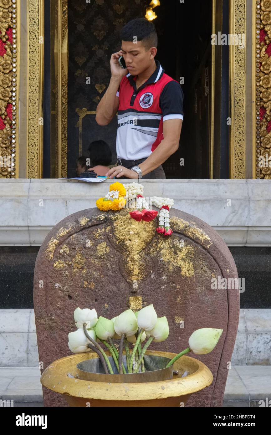 Ein Mann, der am Fenster des (Tempel-)Wat Boworniwet in Bangkok, Thailand, steht, spricht auf seinem Handy, ornamentale Lotusblumen im f/g Stockfoto