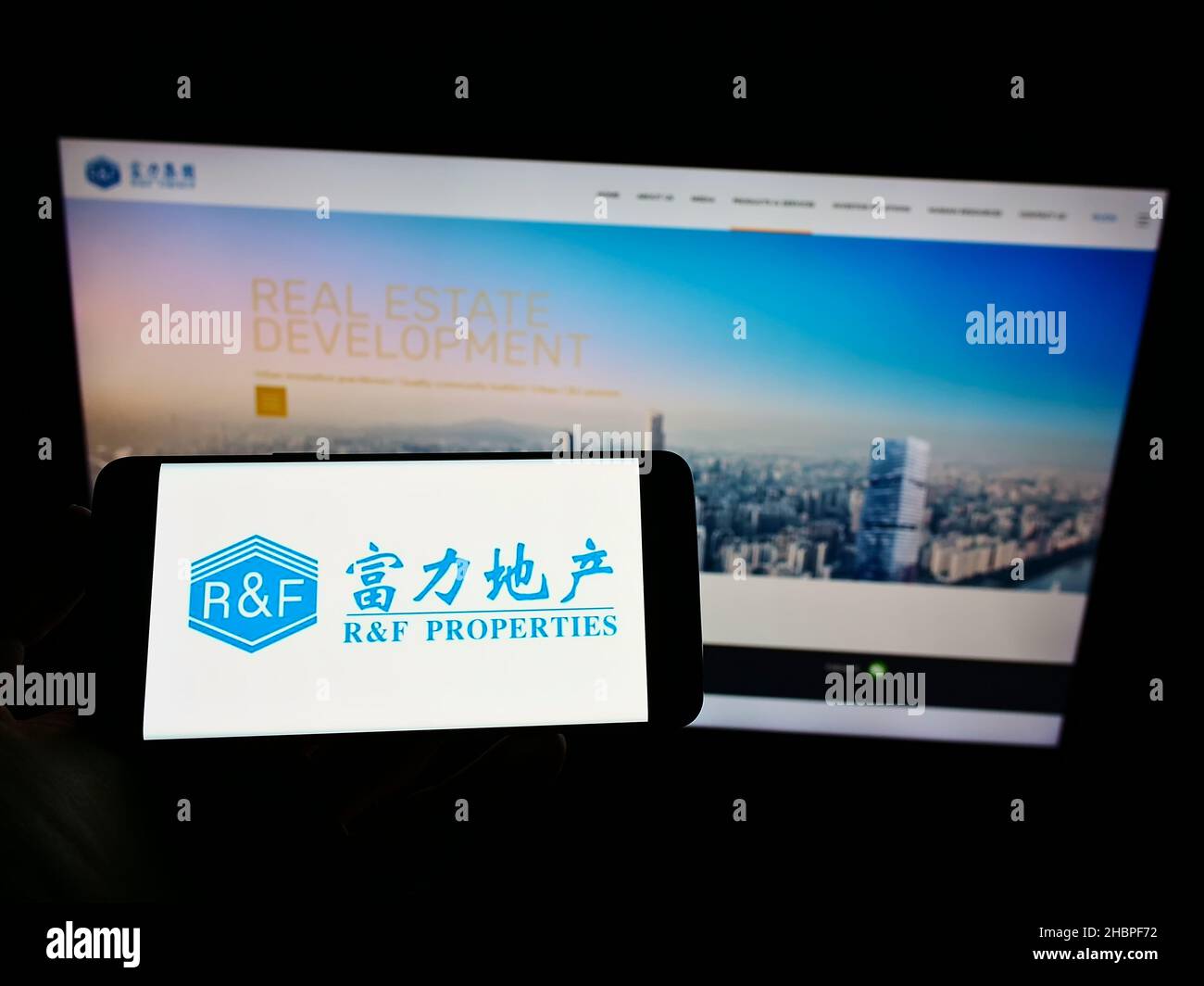 Person, die Mobiltelefon mit Logo der chinesischen Immobiliengesellschaft Guangzhou RF Properties auf dem Bildschirm vor der Webseite hält. Konzentrieren Sie sich auf die Telefonanzeige. Stockfoto