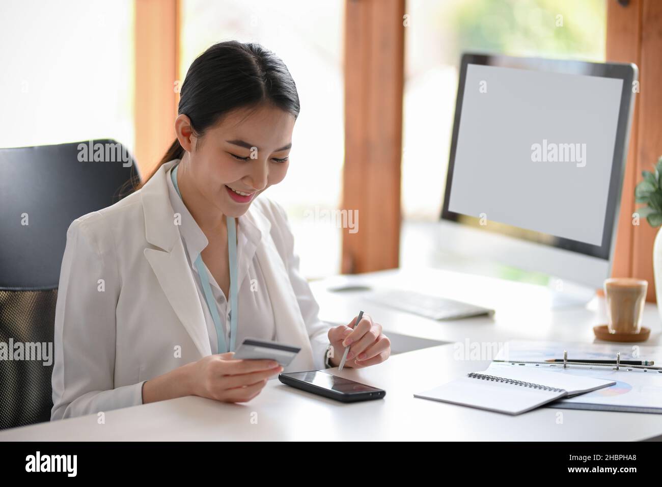 Weibliche Führungskraft oder Unternehmer mit Mobile-Banking-Anwendung, um ihre Rechnungen zu bezahlen, sitzen im modernen Büro. Kreditkarte mit SM Stockfoto