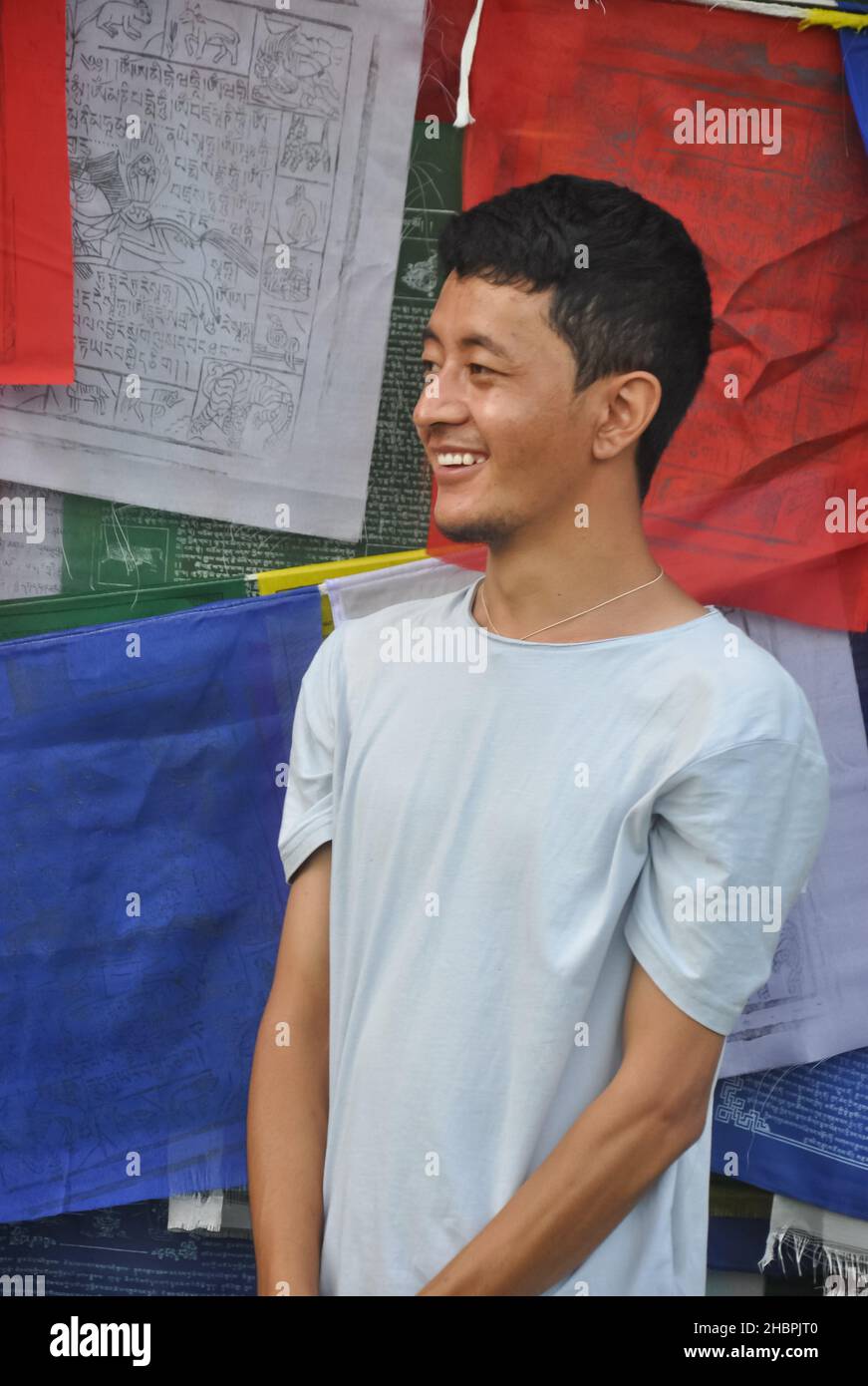 Foto eines asiatischen jungen Mannes, der lächelt und seitwärts schaut, der gegen buddhistische Gebetsfahnen mit Kopierraum steht Stockfoto