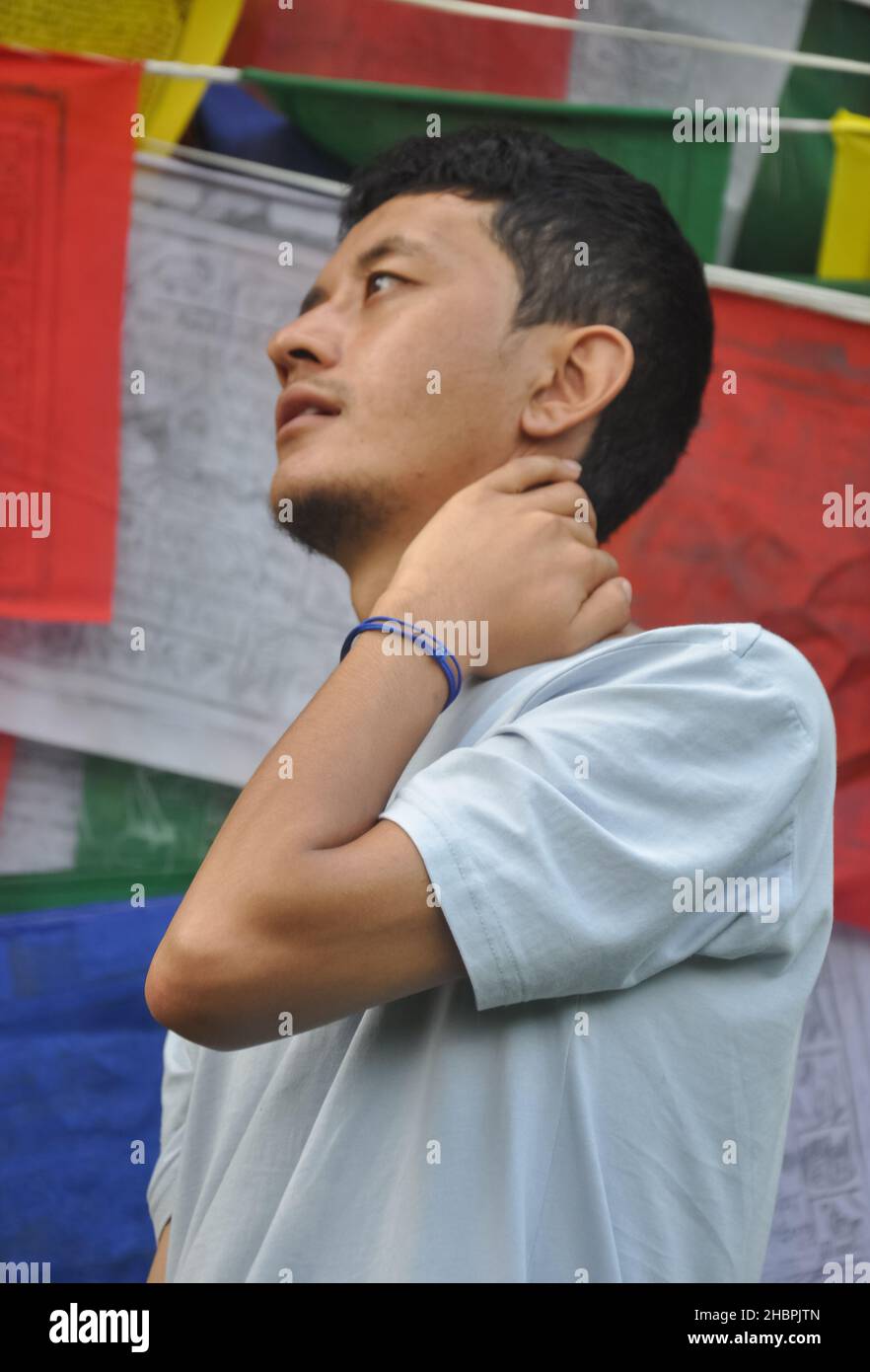 Nahaufnahme eines asiatischen Mannes, der mit der Hand hinter dem Hals zur Seite blickt und gegen buddhistische Gebetsfahnen steht Stockfoto