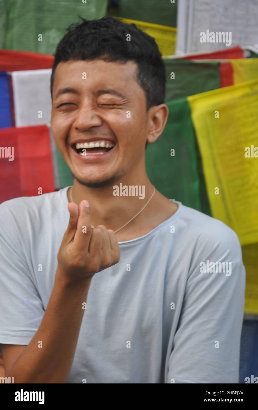 Nahaufnahme eines fröhlichen Tibets, der mit der Hand ein koreanisches Liebeszeichen macht, mit seitlichem Blick gegen buddhistische Gebetsfahnen posiert Stockfoto