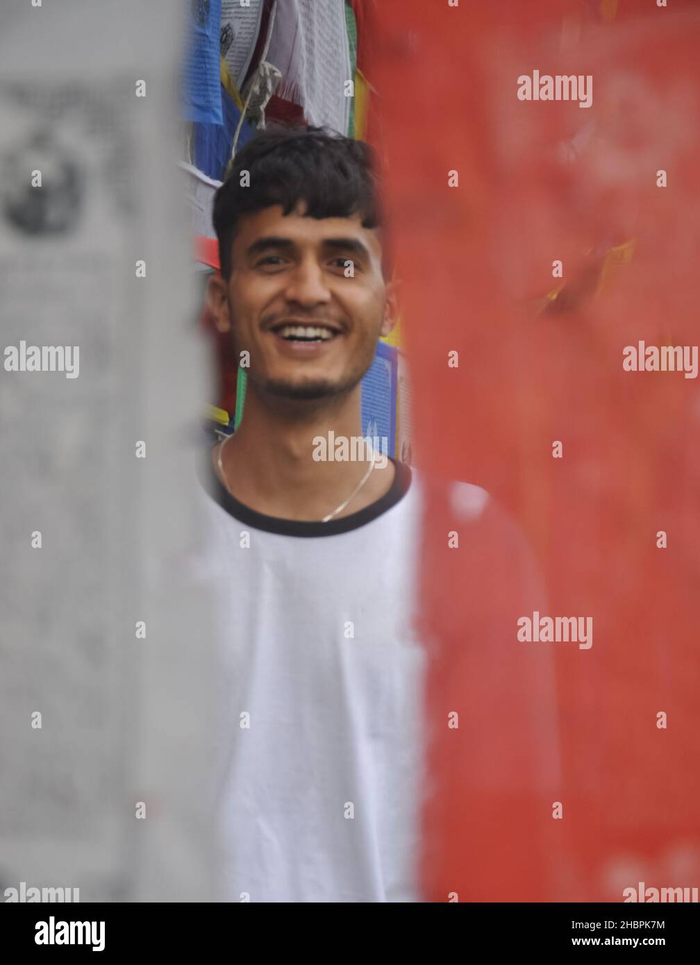Selektiver Fokus eines glücklichen indischen jungen Mannes, der die Kamera anschaut, während er um buddhistische Gebetsfahnen steht Stockfoto