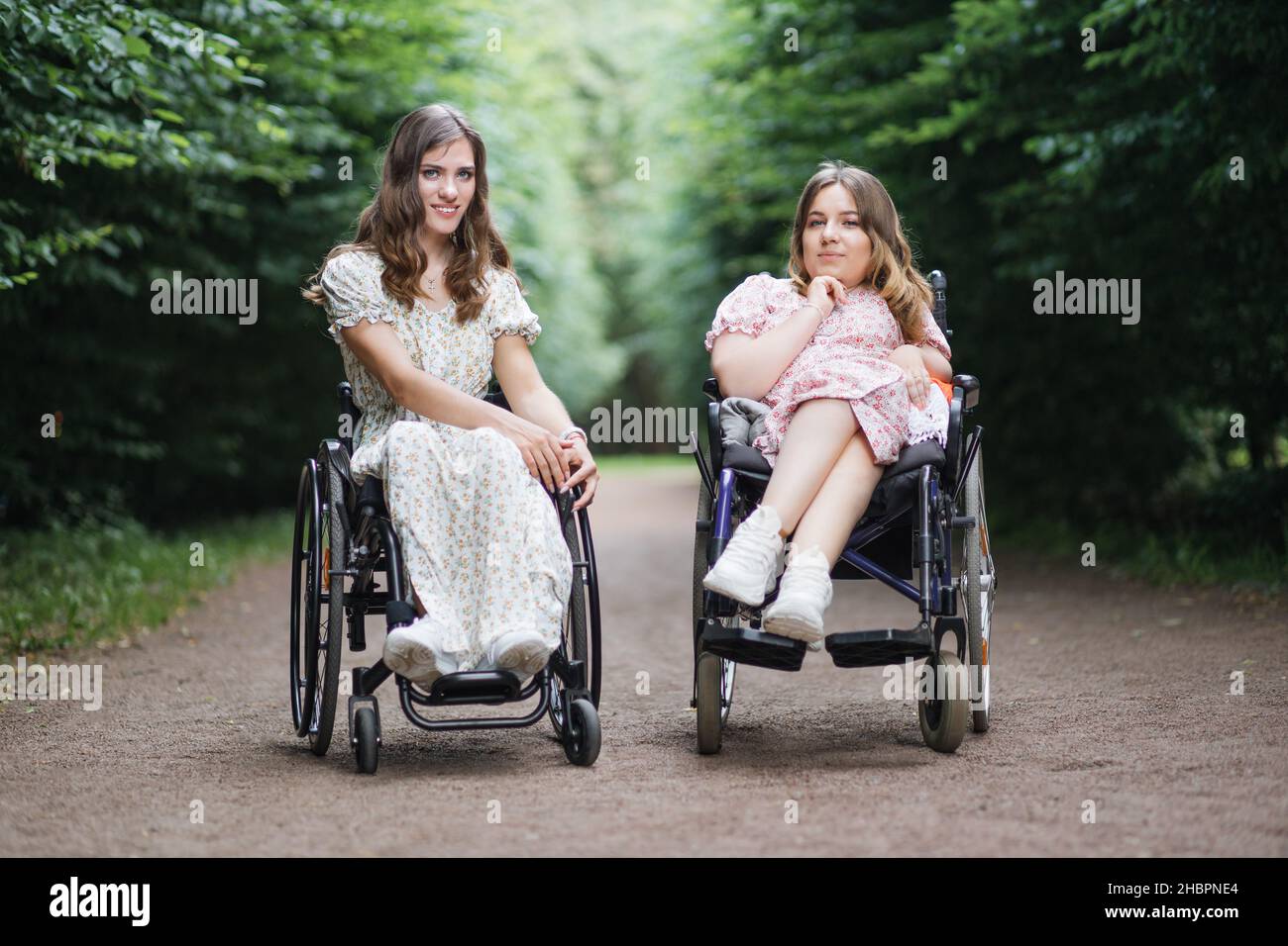 Schöne behinderte Frauen in Sommerkleidern mit Blumenmuster entspannen  zusammen an der frischen Luft. Zwei Freundinnen, die Rollstühle benutzen,  lächeln und blicken in die Kamera Stockfotografie - Alamy