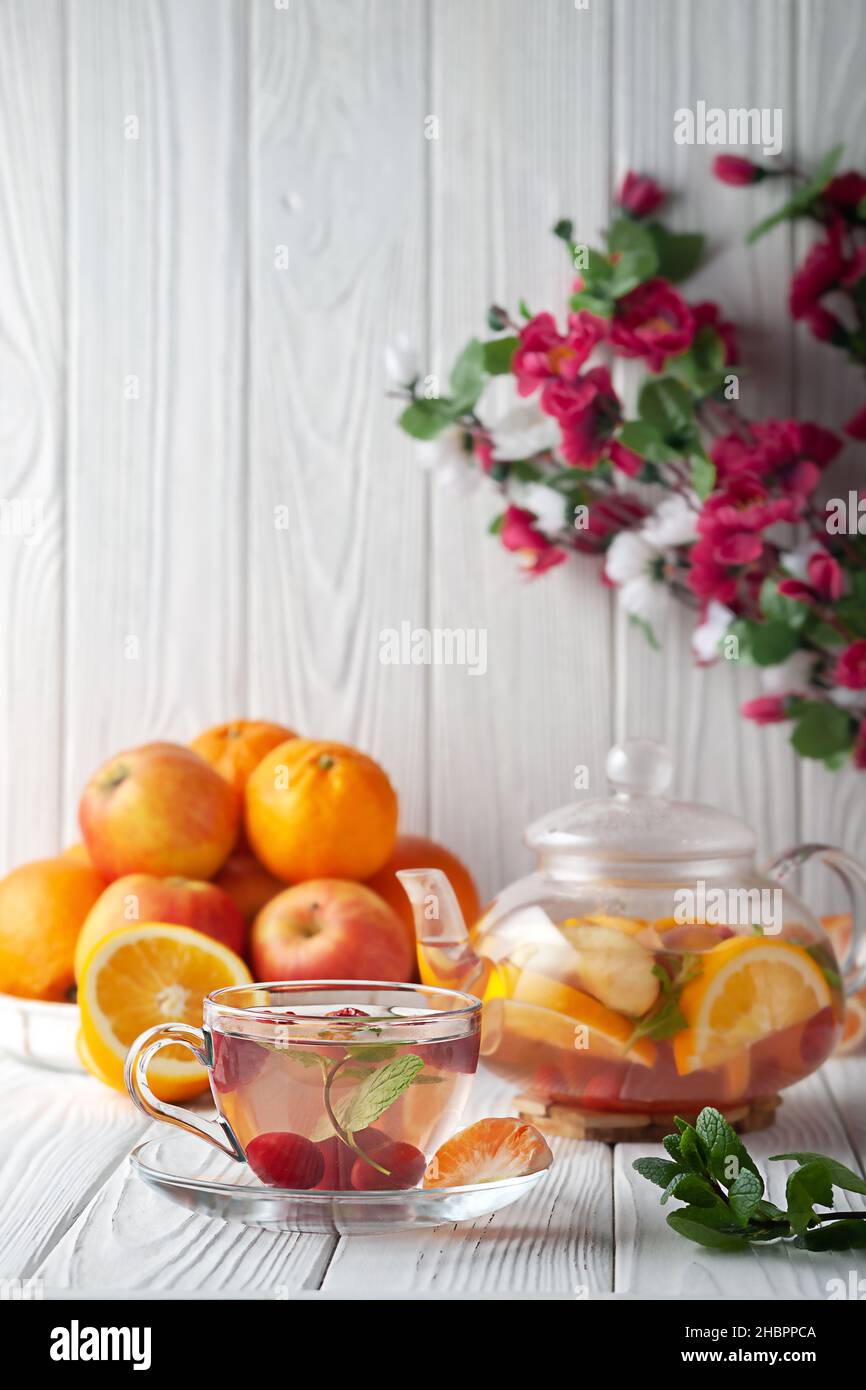 Früchtetee mit Beeren, Orangen und Minze in einer Glas-Teekane auf weißem Holzhintergrund Stockfoto