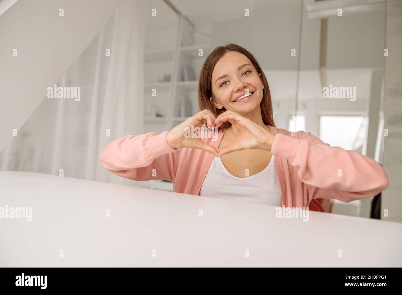 Lächelnde, schöne Dame, die mit ihren eigenen Händen eine Herzform zeigt Stockfoto