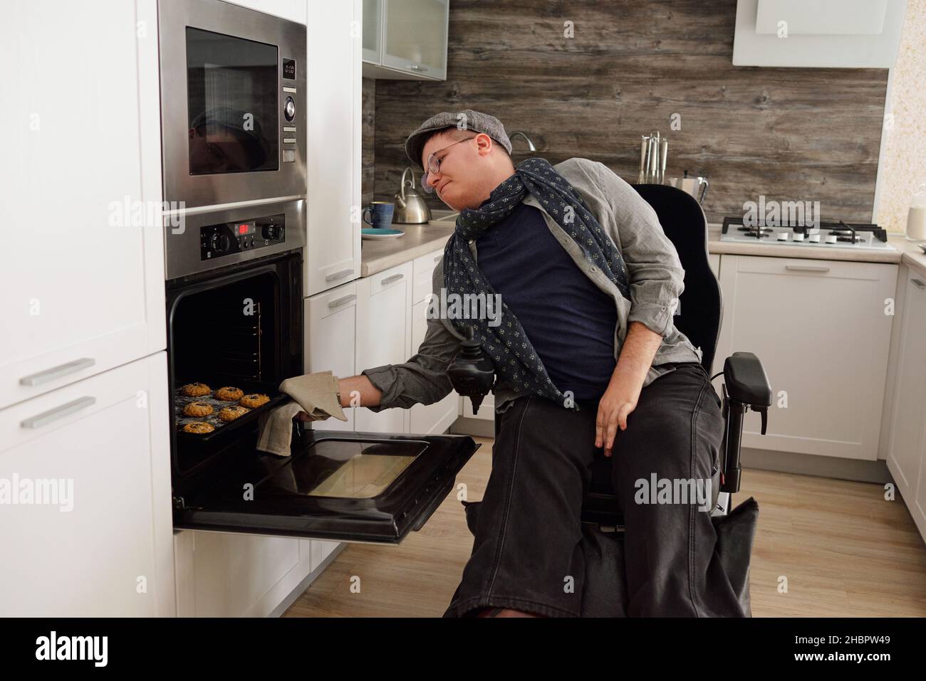 Moderner Mann mit Behinderung, der in der Küche hausgemachte Kekse aus dem Elektroofen nahm Stockfoto