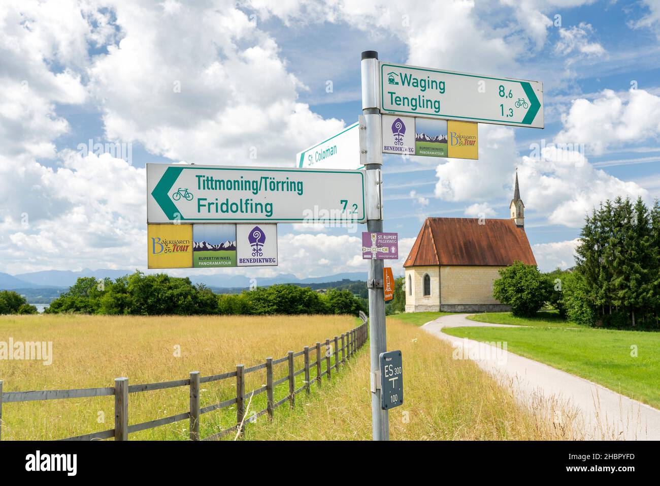 sommerliche Landschaft am Tachinger See mit der Kirche St. Coloman Wegweiser mit Wander- und Radwegbeschilderung Stockfoto