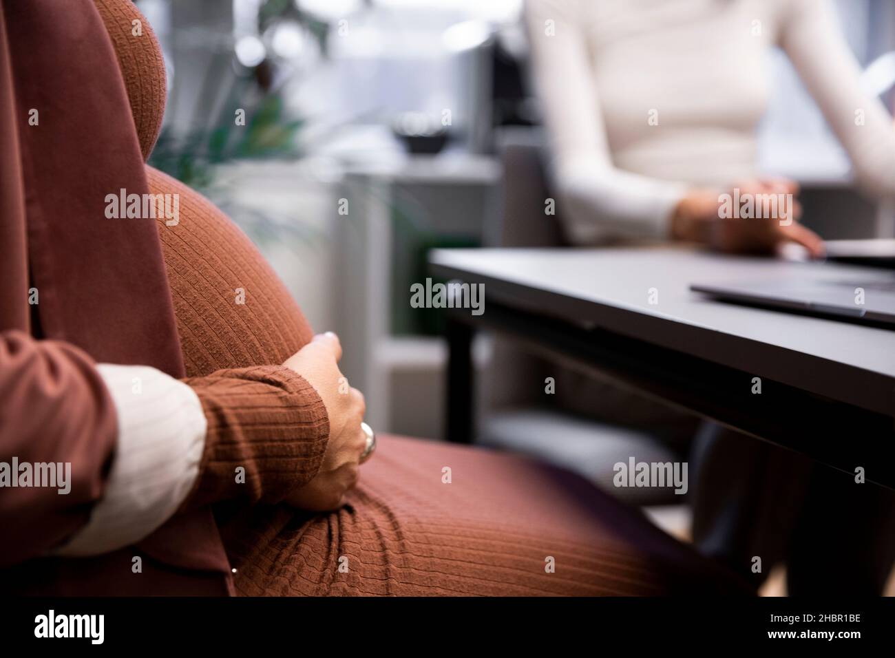 Mittelteil der Schwangeren weiblichen Chefin berührt Bauch, während sie im Büro sitzt Stockfoto