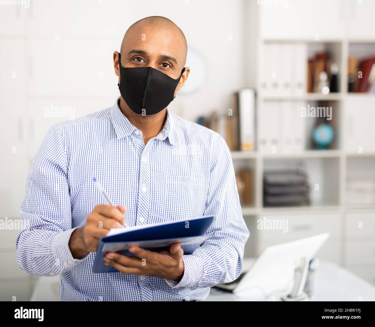 Porträt eines positiven Geschäftsmanns in Schutzmaske mit Dokumentenmappe im Büro Stockfoto
