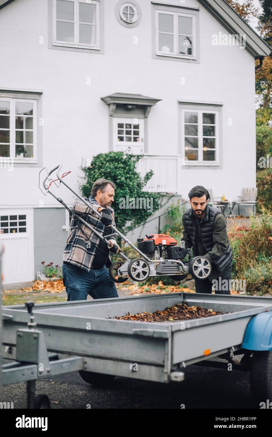 Sohn und Vater beladen Rasenmäher in Fahrzeug Anhänger durch Gebäude Stockfoto