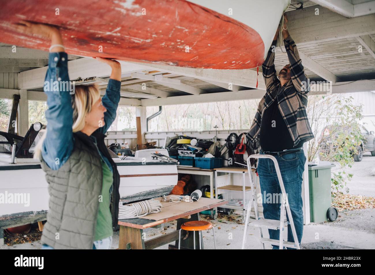 Reifer Mann, der ein nautisches Schiff bindet, während eine Freundin ihm in der Garage hilft Stockfoto