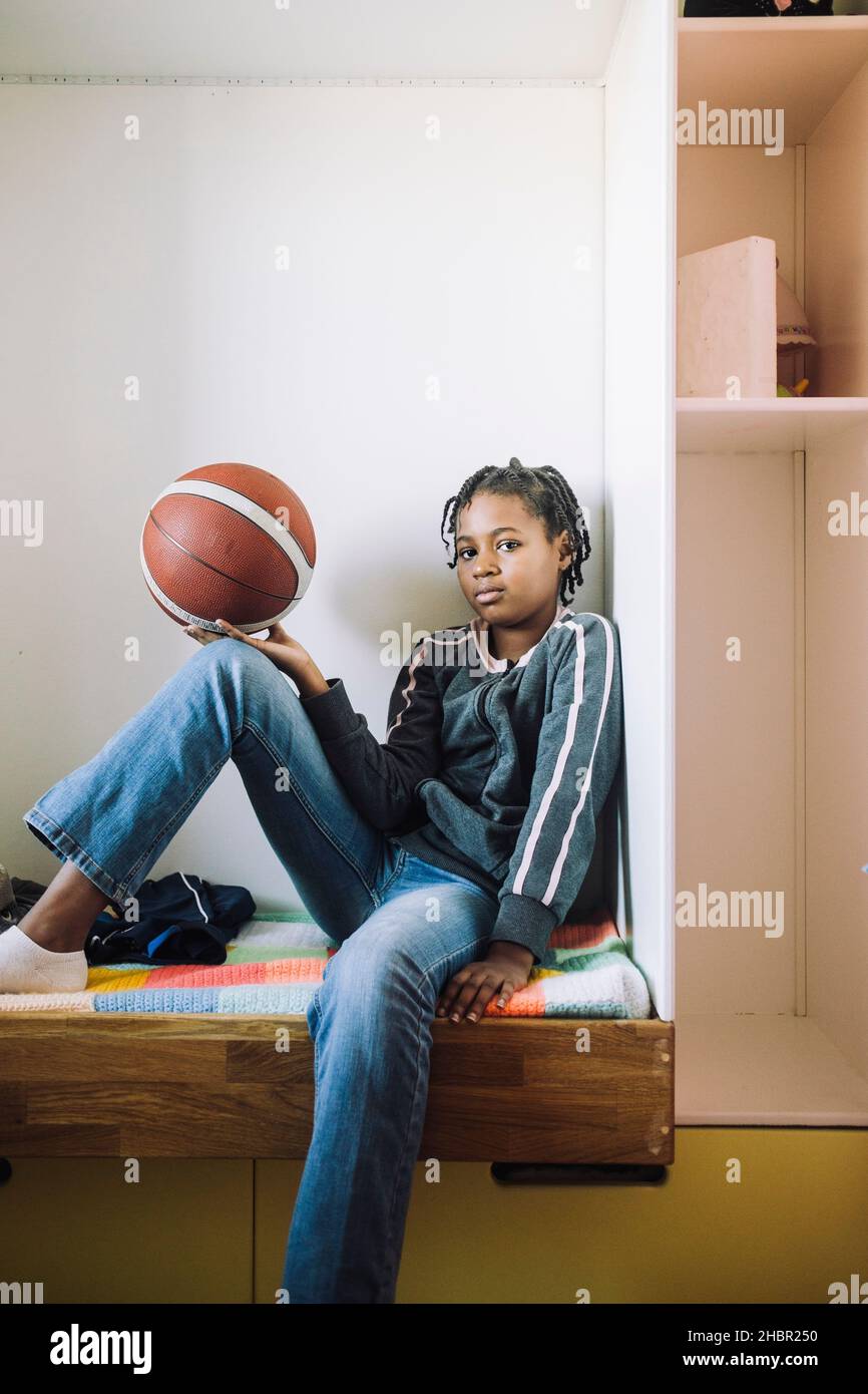 Portrait eines Mädchens mit Basketball, das zu Hause auf dem Bett sitzt Stockfoto