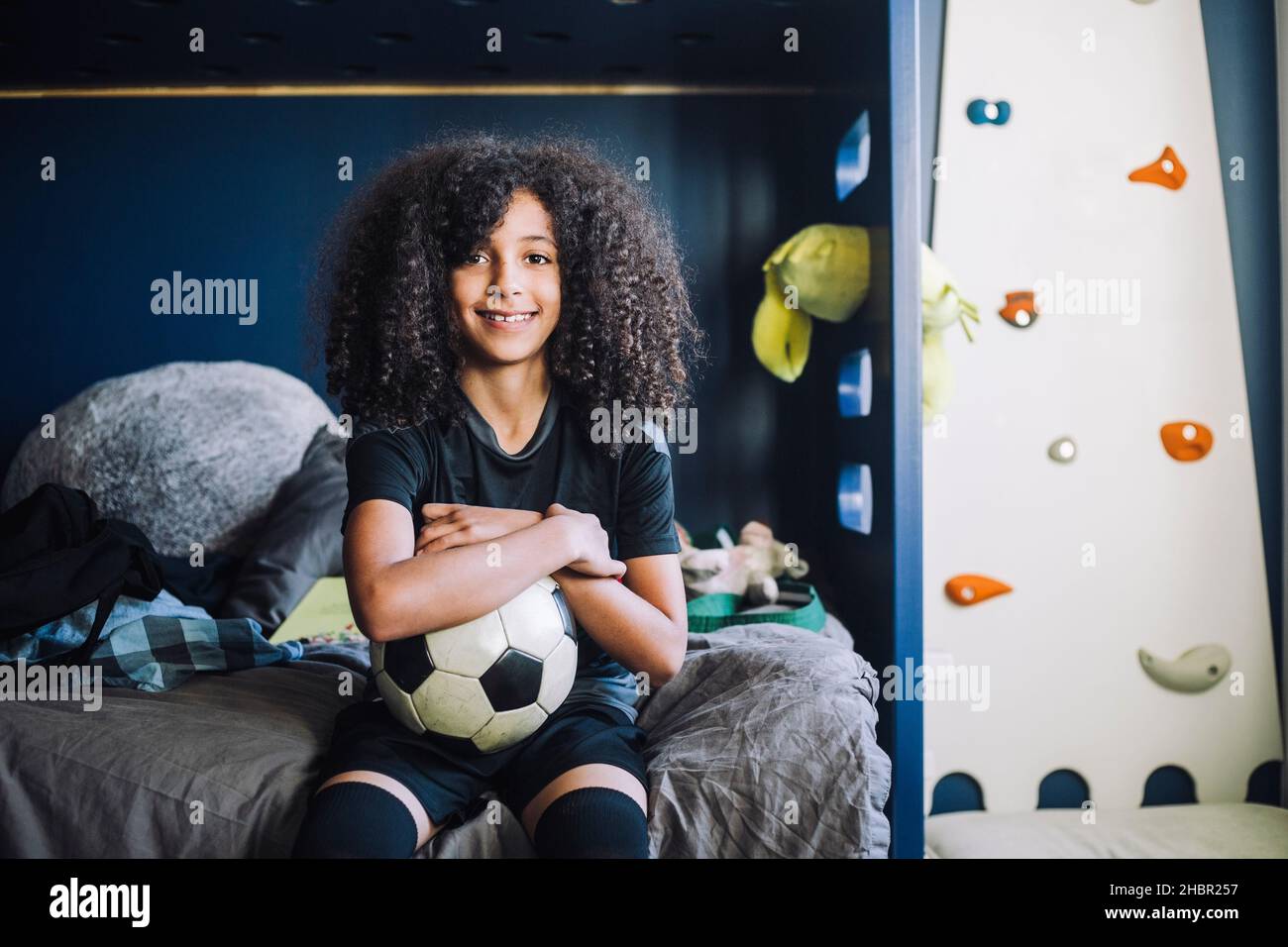 Porträt eines Mädchens mit Fußball, das im Schlafzimmer auf dem Bett sitzt Stockfoto