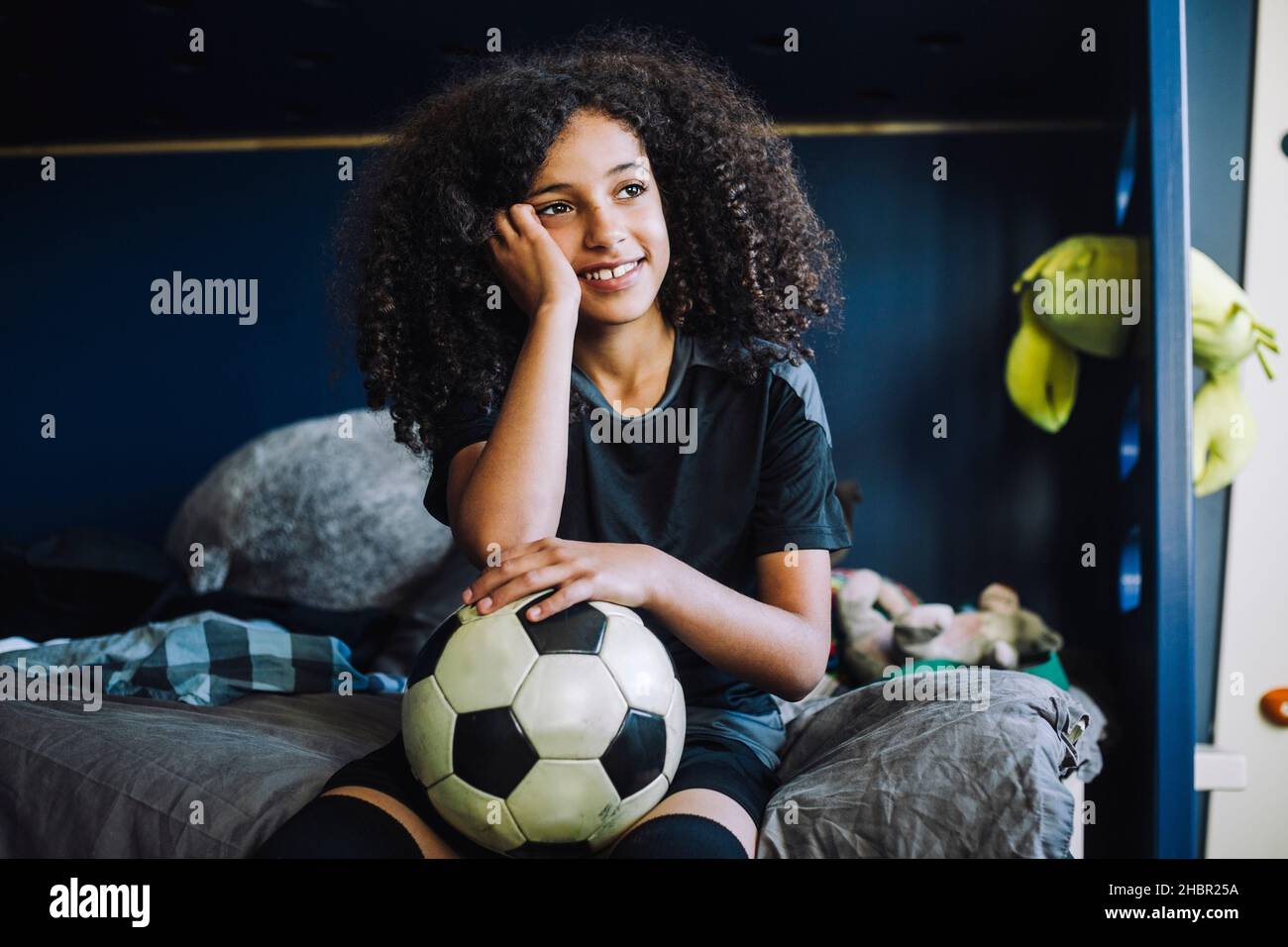 Mädchen kontempliert mit Fußball im Schlafzimmer Stockfoto