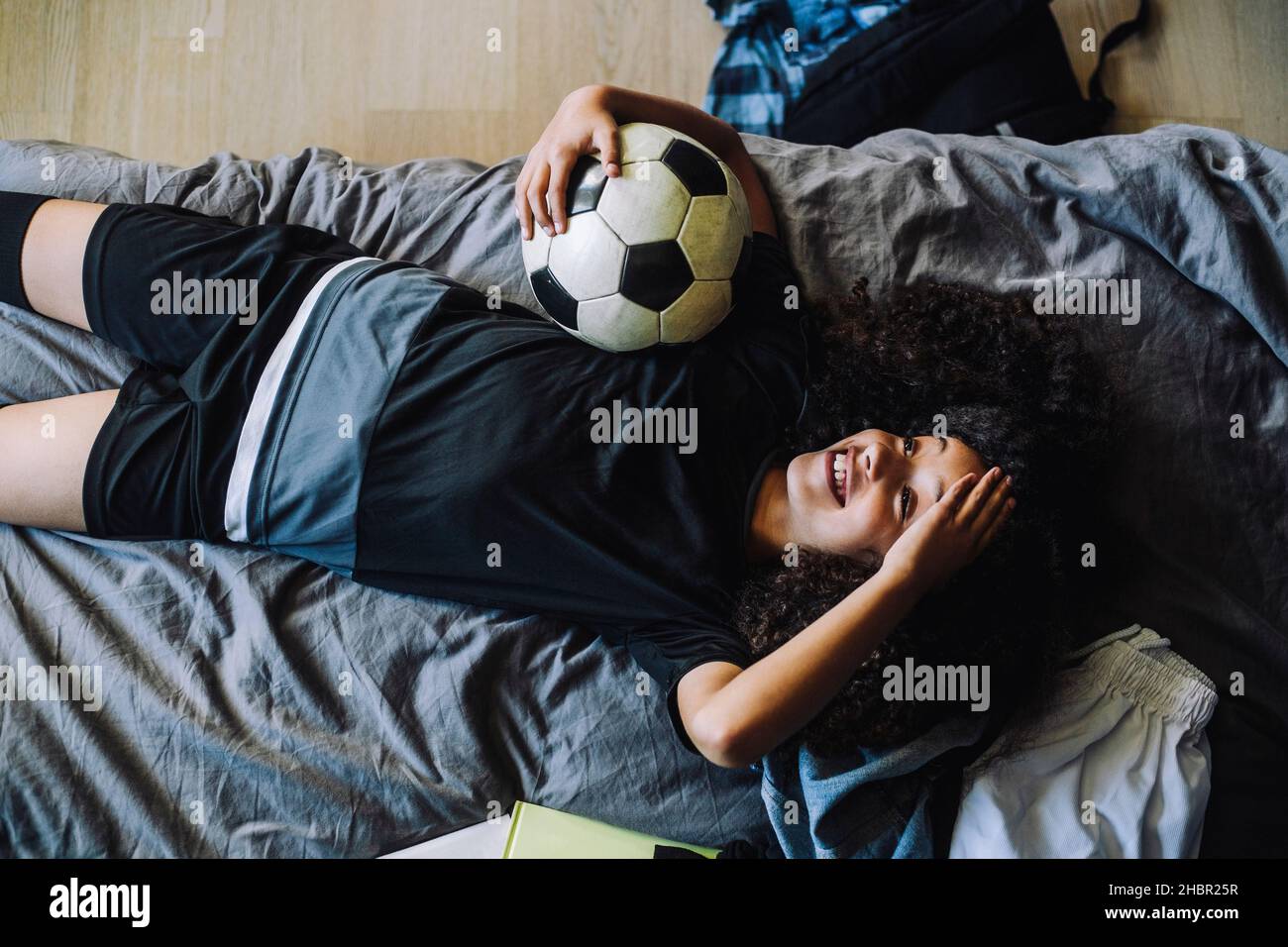 Direkt über der Aufnahme eines lächelnden Mädchens mit Fußball, der auf dem Bett lag Stockfoto