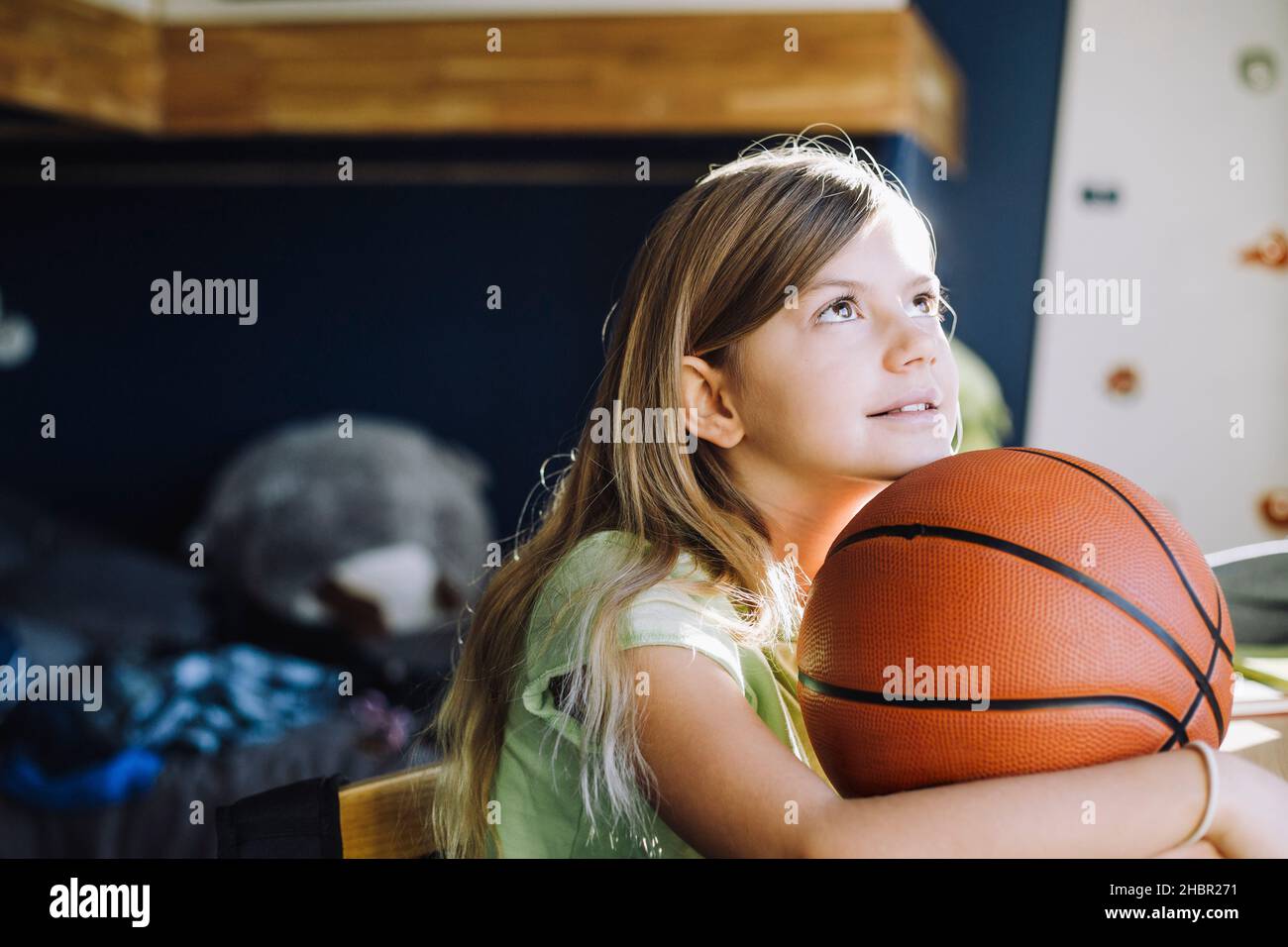 Mädchen, die aufschaut, während sie zu Hause mit Basketball sitzt Stockfoto