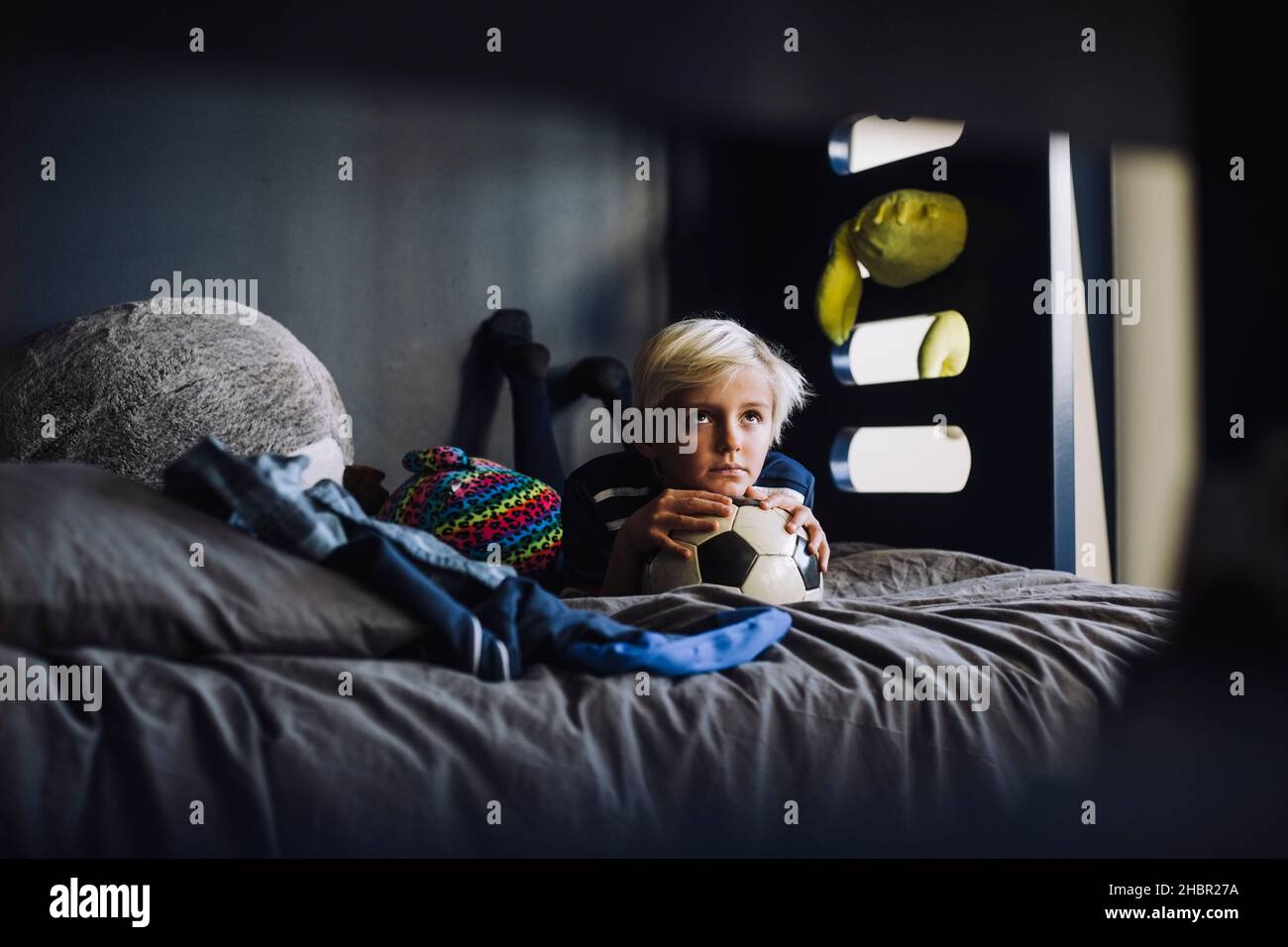 Beschaulicher Junge mit Fußball, der zu Hause auf dem Bett liegt Stockfoto