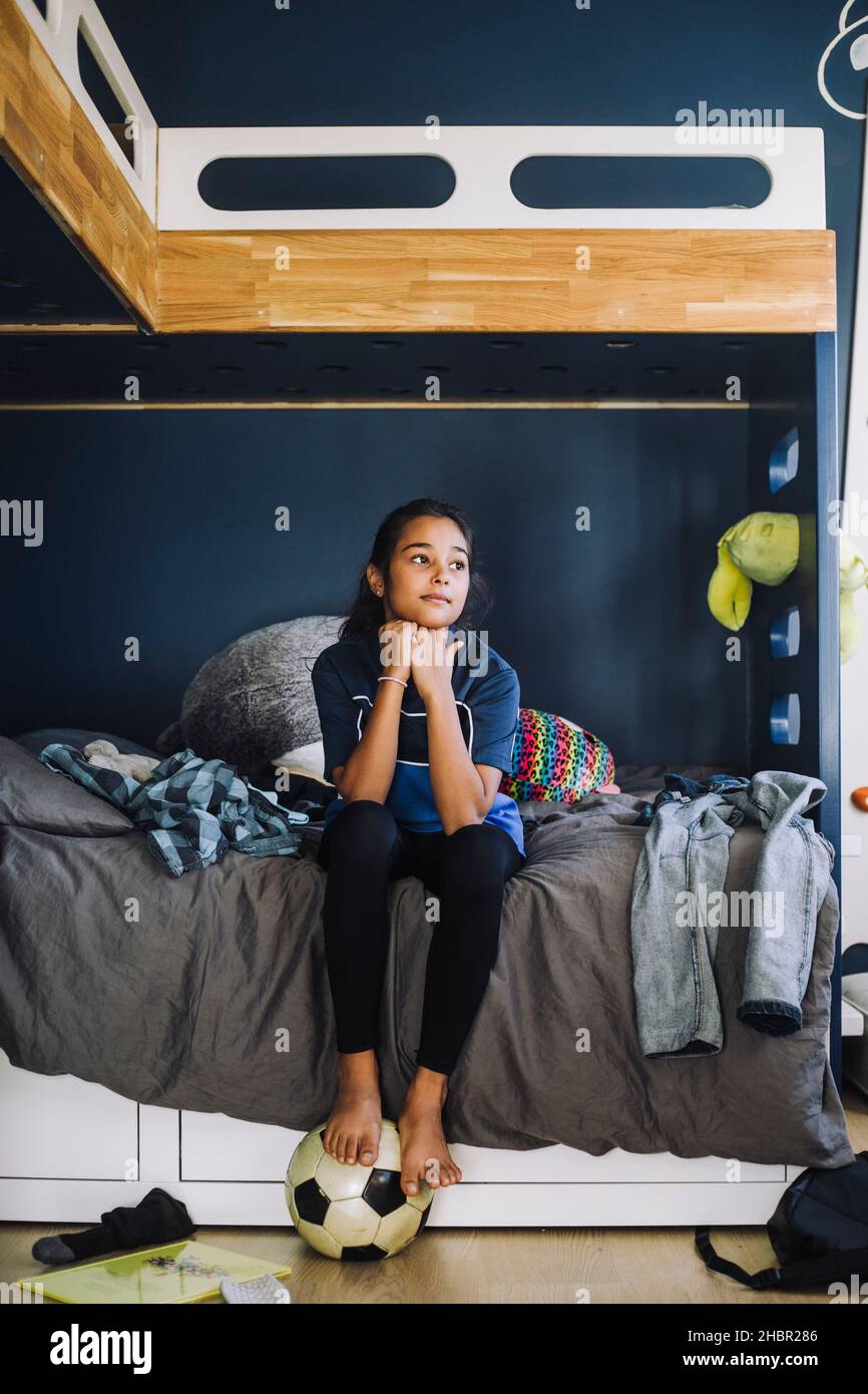 Mädchen mit der Hand auf dem Kinn Kontemplation in chaotisch Schlafzimmer Stockfoto