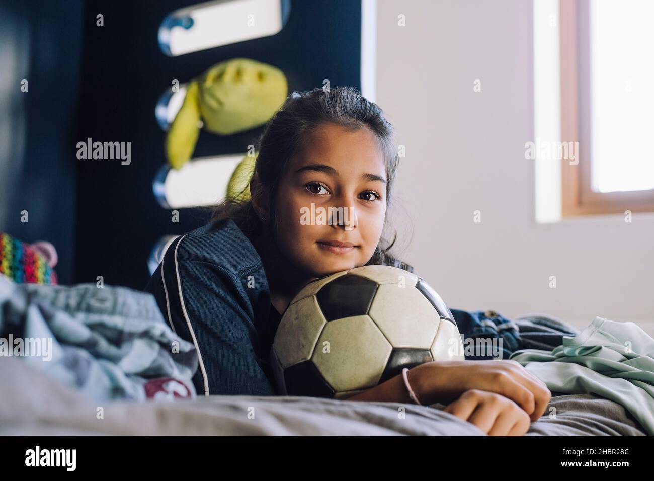 Porträt eines Mädchens mit Fußball, das zu Hause auf dem Bett liegt Stockfoto