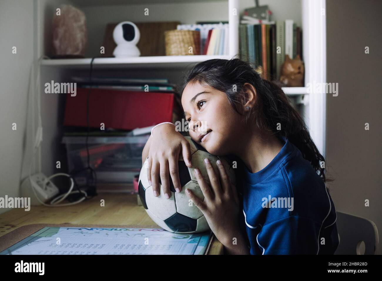 Kontemplatives Mädchen, das mit Fußball am Tisch wegschaut Stockfoto