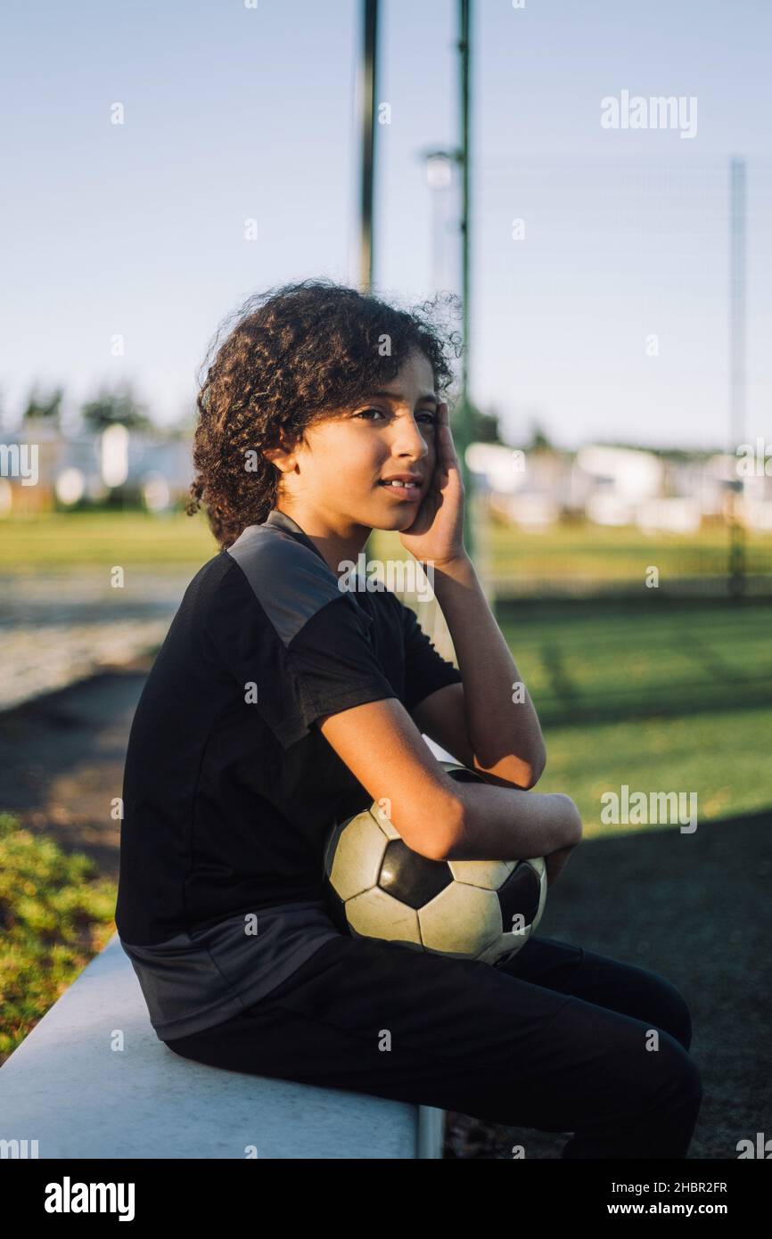 Weibliche Athletin mit Fußball sitzt auf Stützwand Stockfoto