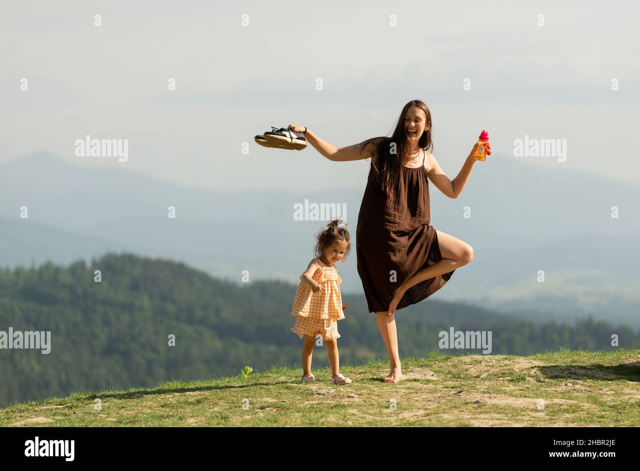 Lächelnde Mutter mit kleiner Tochter, die Yoga macht und am Berg spielt. Stockfoto