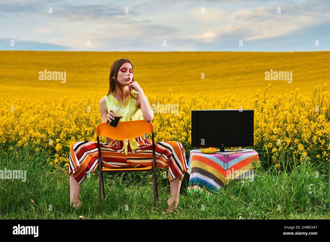 Mädchen sitzt auf einem Stuhl mit einem Getränk auf dem Feld Stockfoto