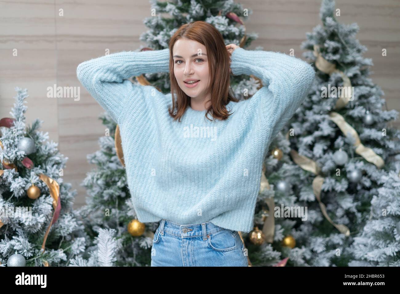 Neujahrsbild der schönen lächelnden kaukasischen jungen Frau in gemütlicher Wolle warm hellblau Pullover stehen in der Nähe geschmückt Weihnachtsbaum. Glückliche Person Stockfoto