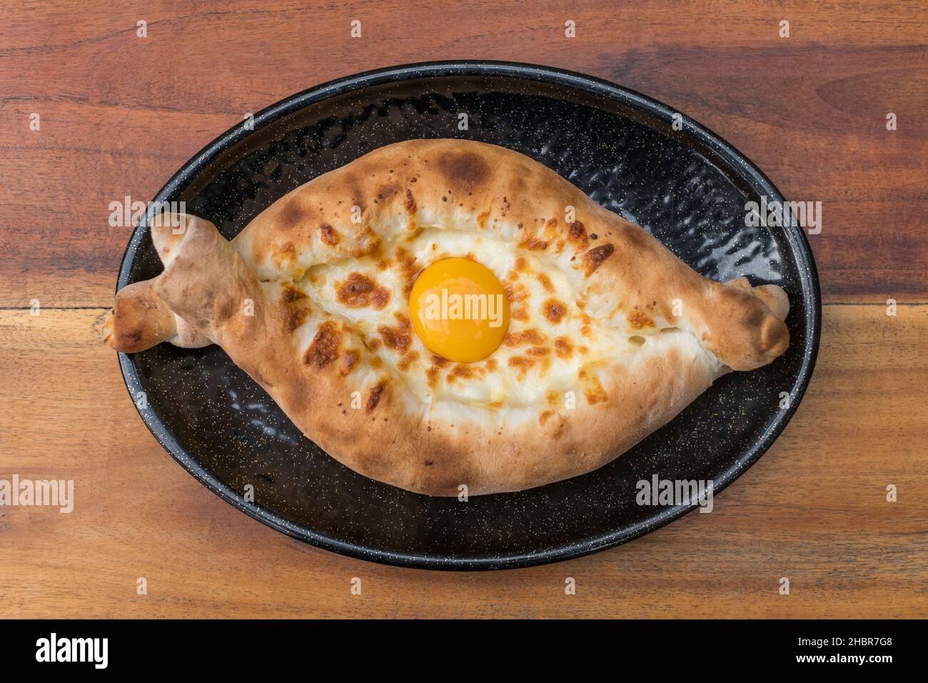 Traditionelle georgische Küche. Ajara khachapuri mit Ei auf schwarzem Teller auf Holzhintergrund Draufsicht, Nahaufnahme mit Kopierraum. Hochwertige Fotos Stockfoto