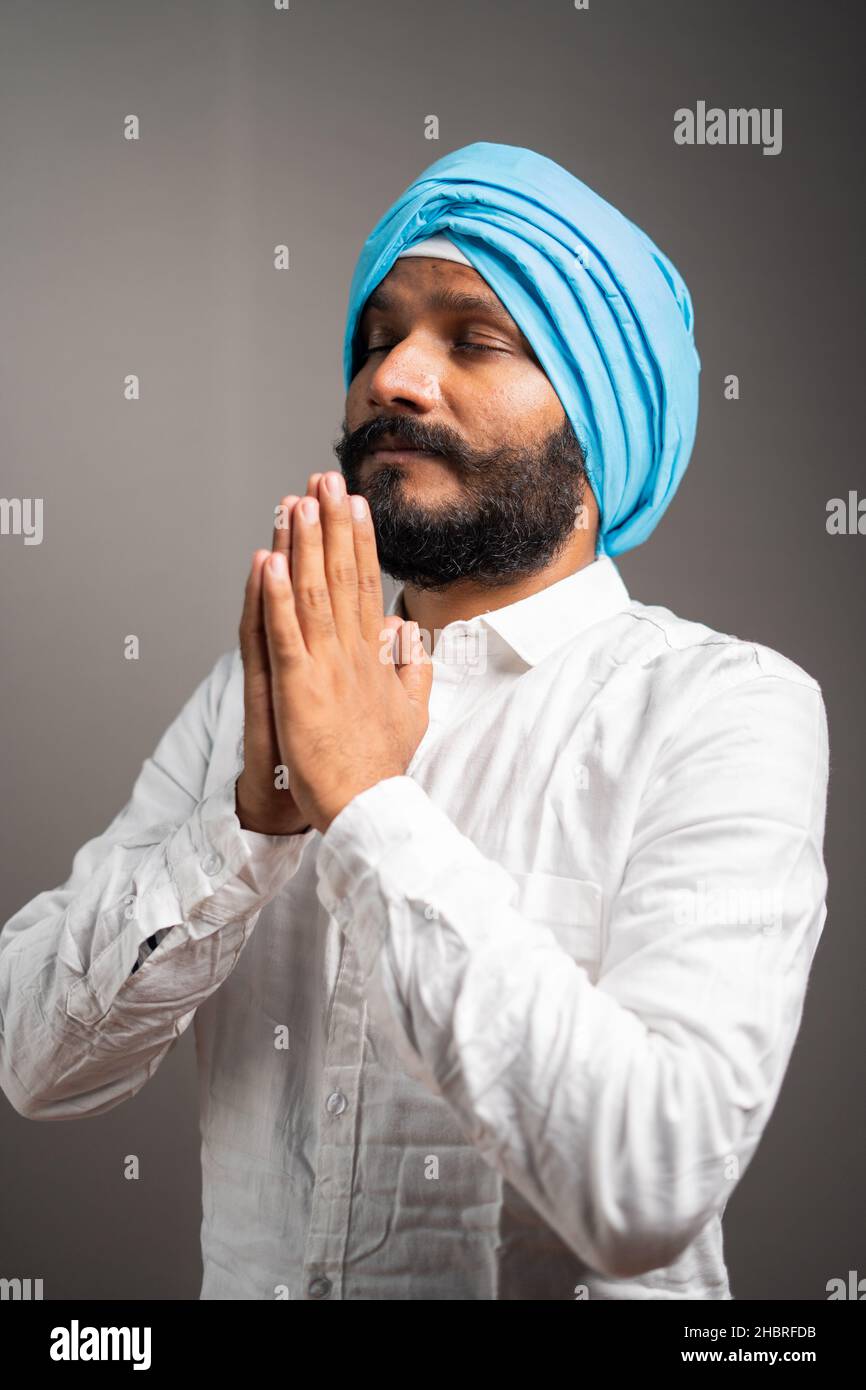 Seitenansicht eines indischen sikh-Mannes, der auf grauem Hintergrund mit geschlossenen Augen Namste tut oder zu gott betet - Glaubensbekenntnis, religiöse Überzeugungen und Sikhismus Stockfoto