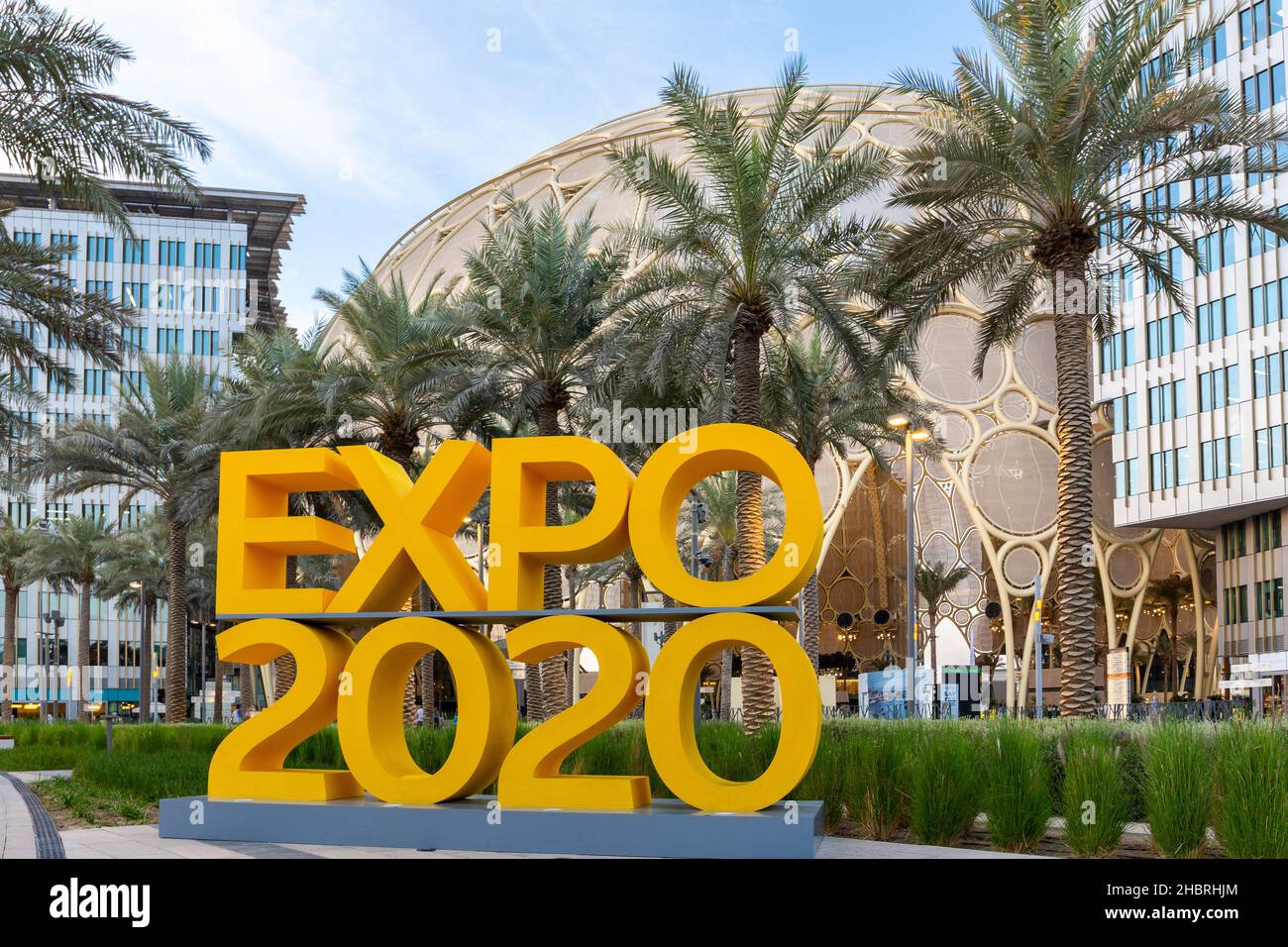 Dubai, VAE, 09.12.2021. Gelbes Logo der Expo 2020 auf der Expo 2020 Dubai mit Al Wasl Plaza und Palmen im Hintergrund. Stockfoto