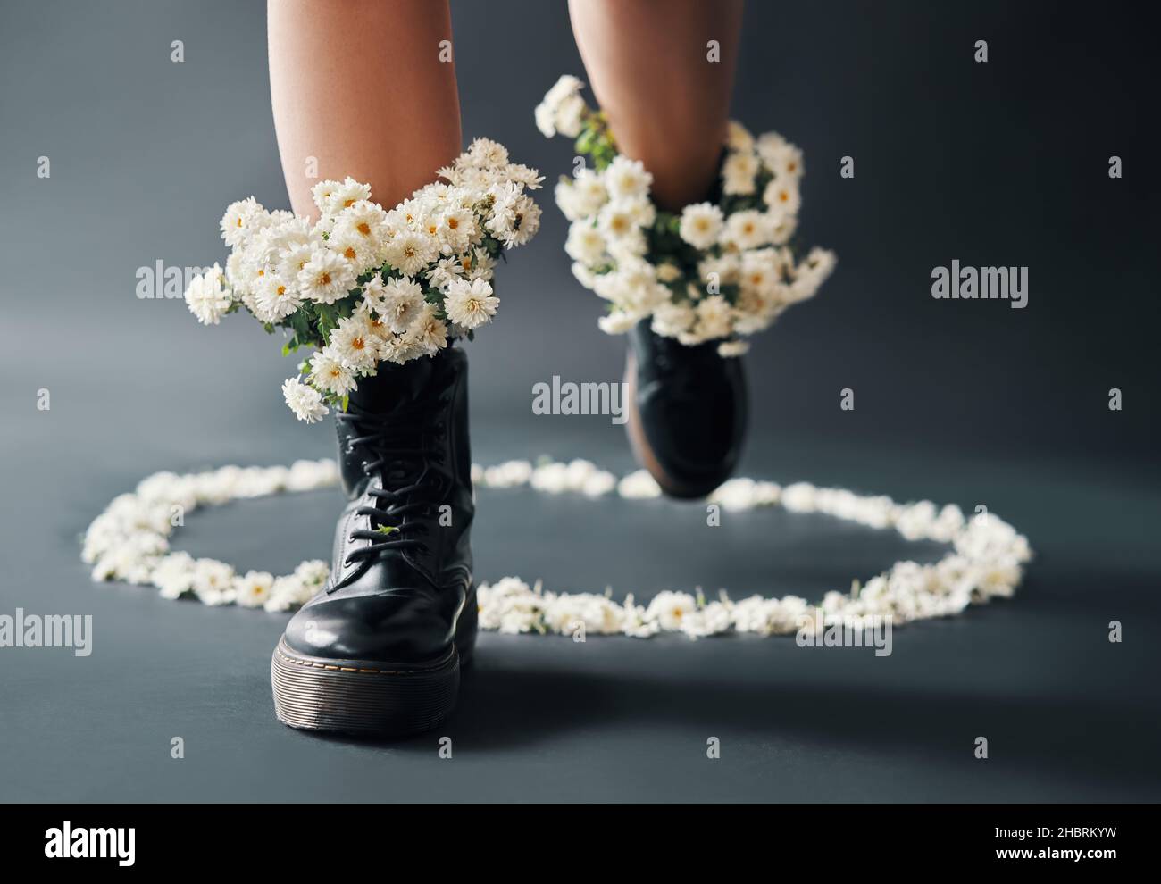 Weibliche Beine in Stiefeln mit blühenden weißen Blüten im Inneren treten aus dem Komfortzonenkreis. Kreativ, Erfolg und Überwindung von Hindernissen Konzept. Stockfoto