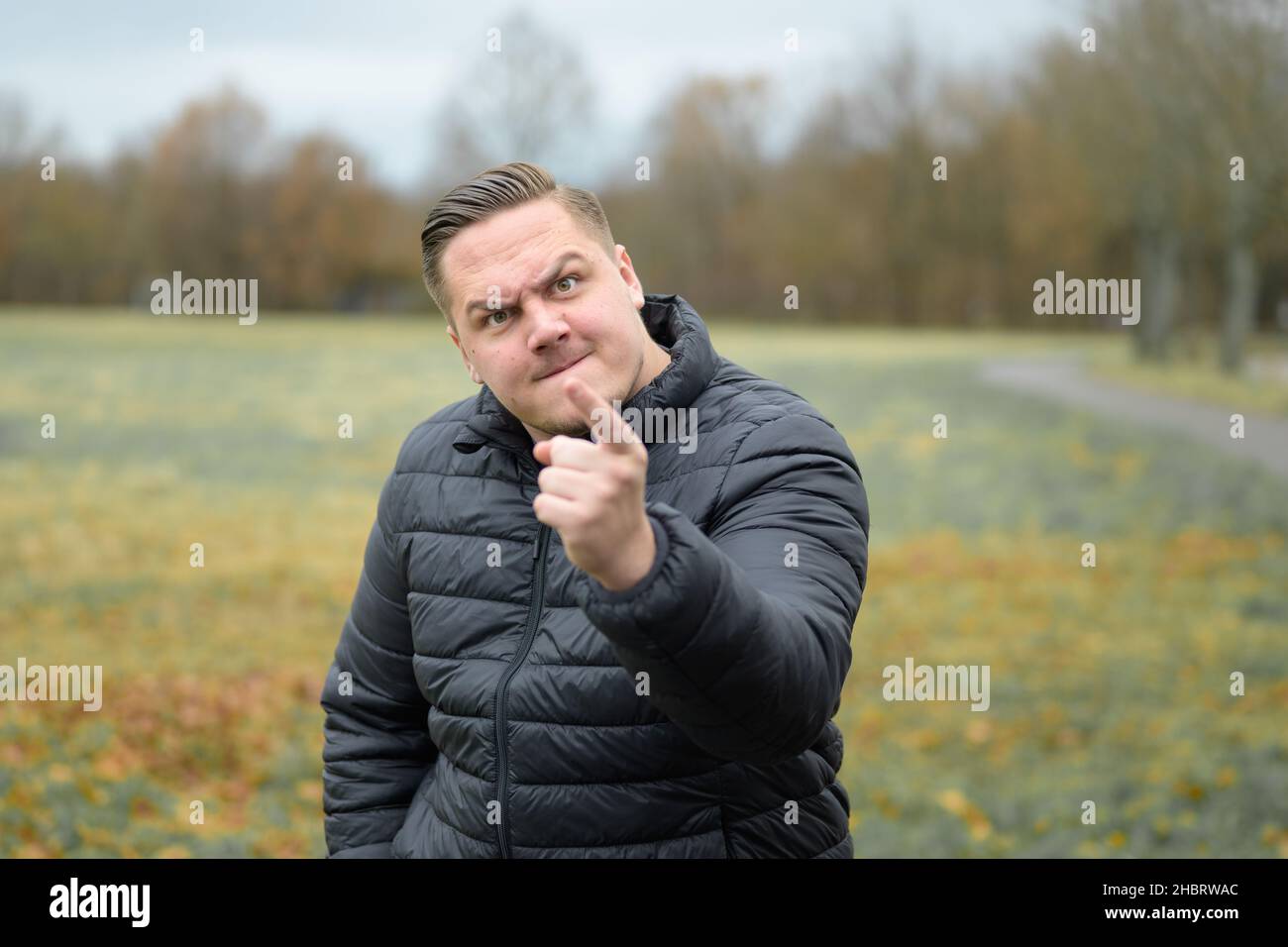 Streitlustig aggressiver junger Mann, der den Zuschauer bedroht und mit einem bärigen Blendlicht auf den Finger zeigt Stockfoto