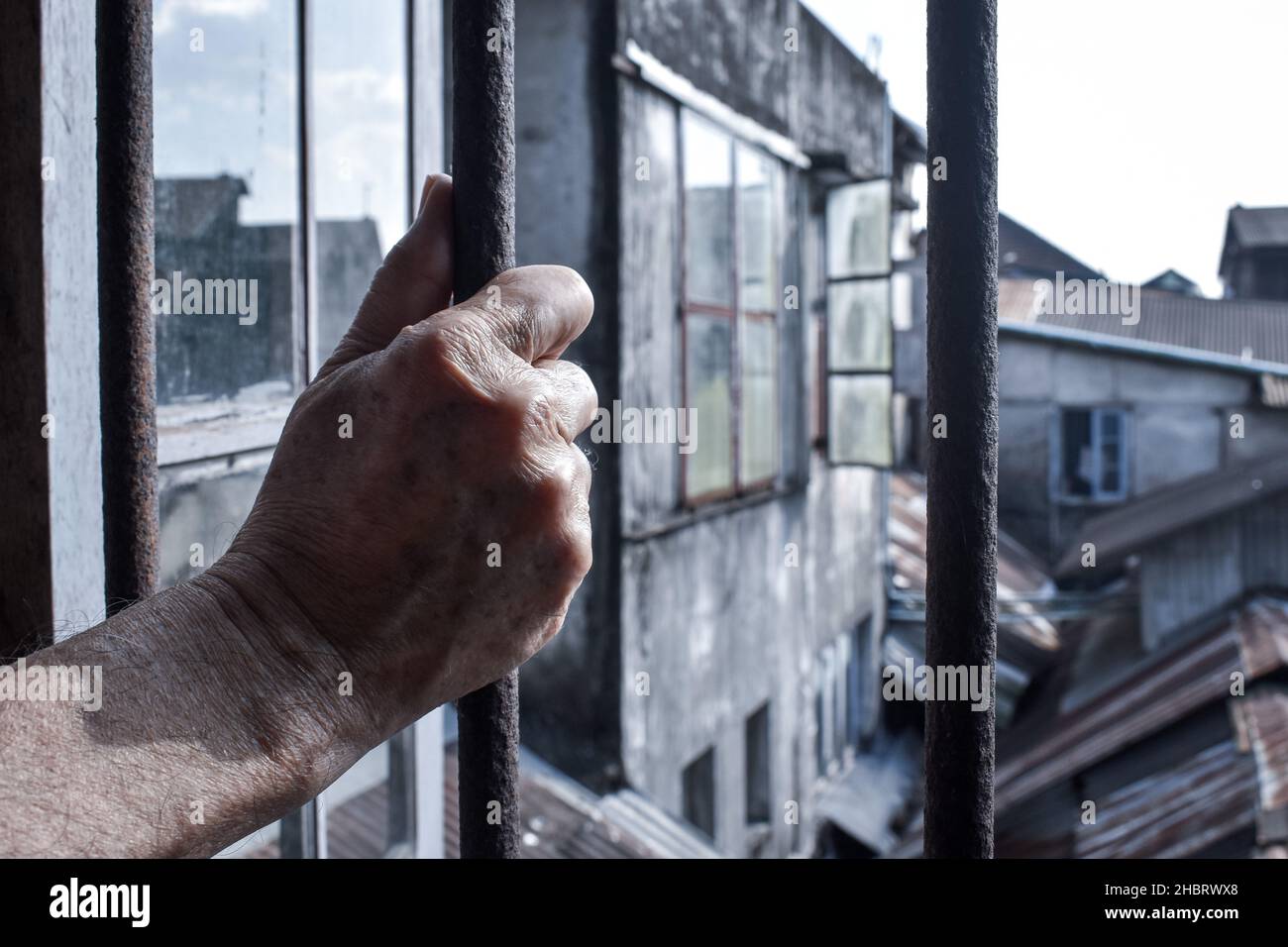 Die Hand eines älteren Mannes aus Asien hält einen eisernen Fensterstock. Konzept von älterer Einsamkeit, sozialer Isolation und mentalem Trauma. Stockfoto