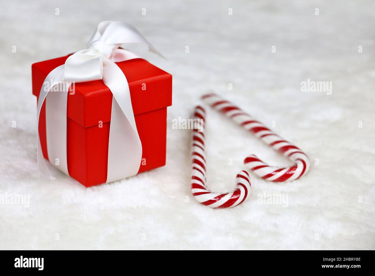 Rote Geschenkbox mit weißer Schleife und Weihnachtsbonbons auf dem Pelzteppich. Romantisches Geschenk für Neujahr oder Valentinstag Stockfoto