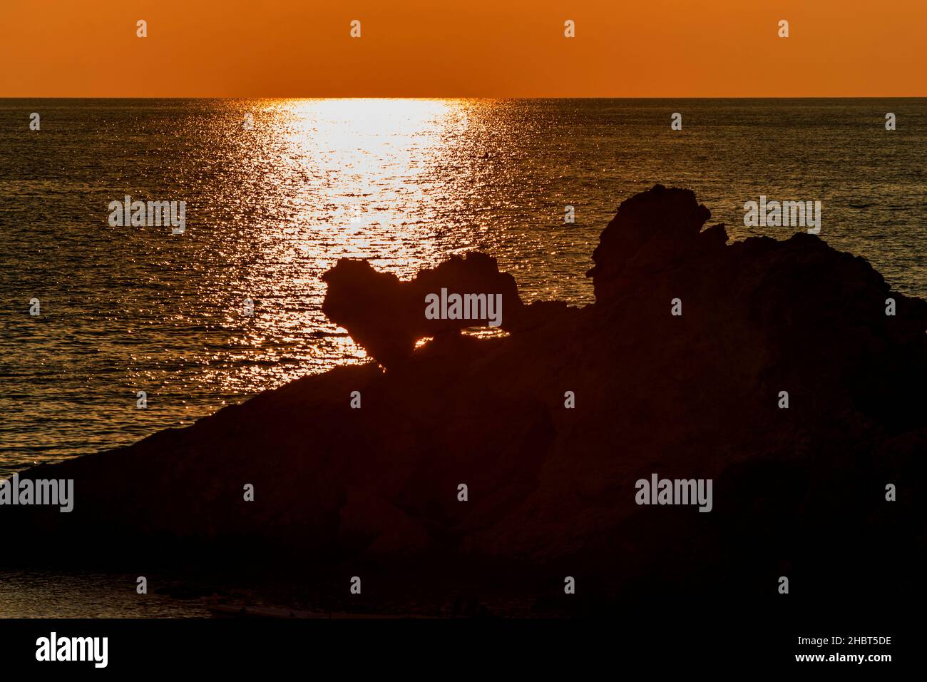 Dunkle Silhouette von Felsküste, funkelndes Meer bei Sonnenuntergang und schöne orange Farbe des Himmels. Limnos, Griechenland. Stockfoto