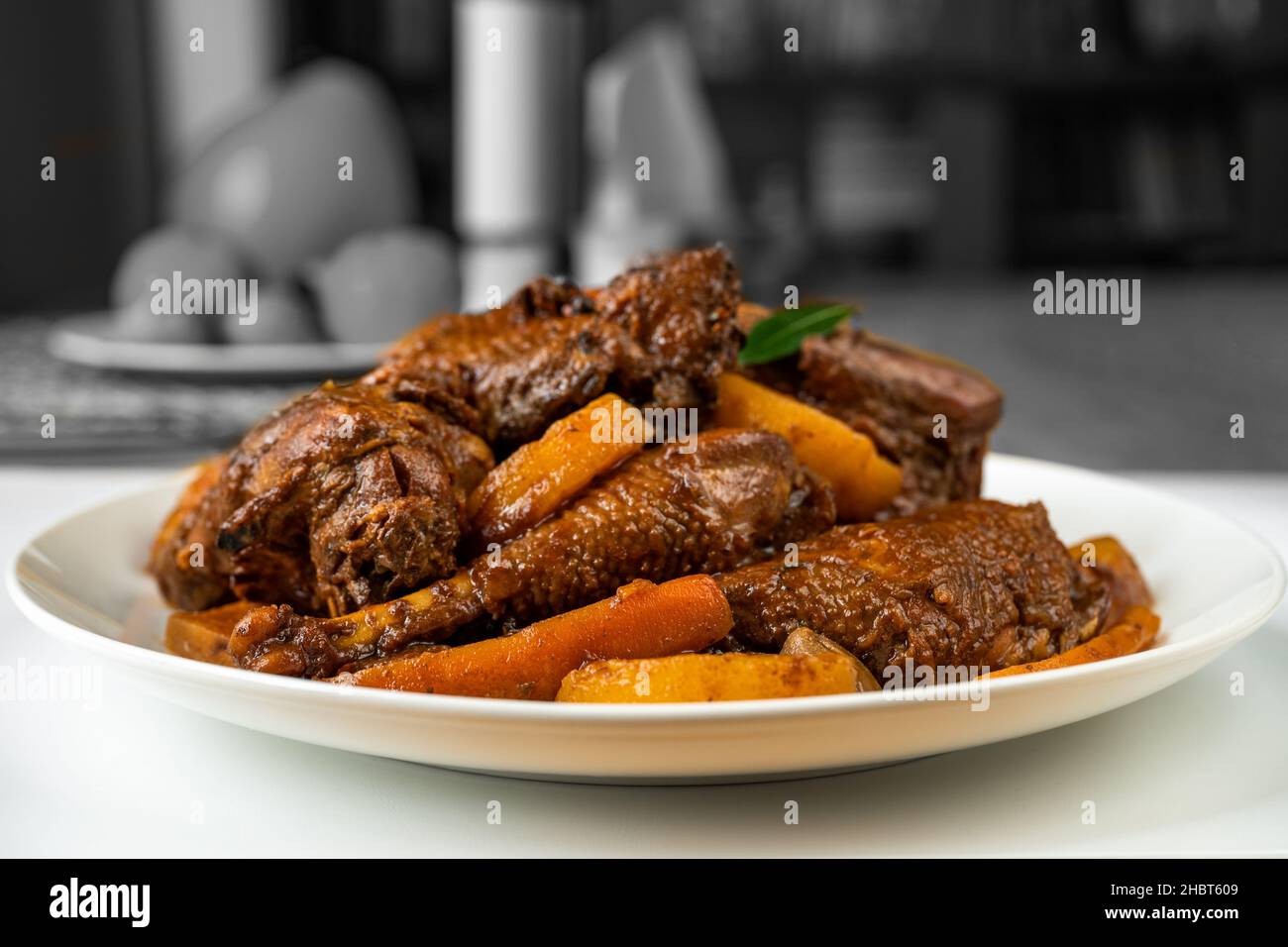 Gebackene Henne, viele Stück mit Gemüse und Birne auf dem Teller auf dem Tisch, hinten in schwarz-weißer Farbe. Altböhmische Spezialität, Nahaufnahme. Stockfoto