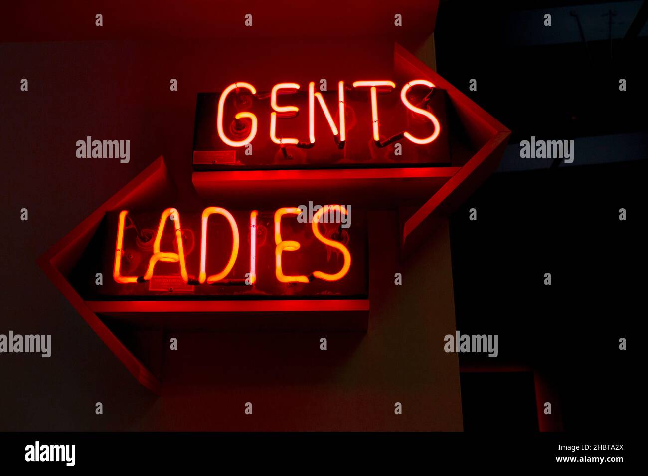 Toilettenschilder für Damen und Herren in roten Neon-Neonfarben kommentieren das geschlechtsspezifische Toilettenkonzept mit Pfeilen, die in andere Richtung zeigen Stockfoto