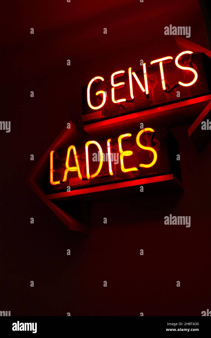 Toilettenschilder für Damen und Herren in roten Neon-Neonfarben kommentieren das geschlechtsspezifische Toilettenkonzept mit Pfeilen, die in andere Richtung zeigen Stockfoto