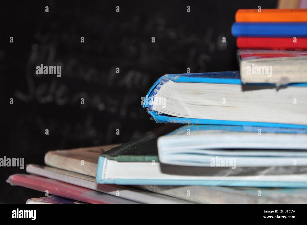 Stapel von Büchern mit Notizen Papier auf Holztisch mit Kreidetafel im Hintergrund.Stapel von Büchern auf Holztisch mit Tafel Hintergrund Stockfoto