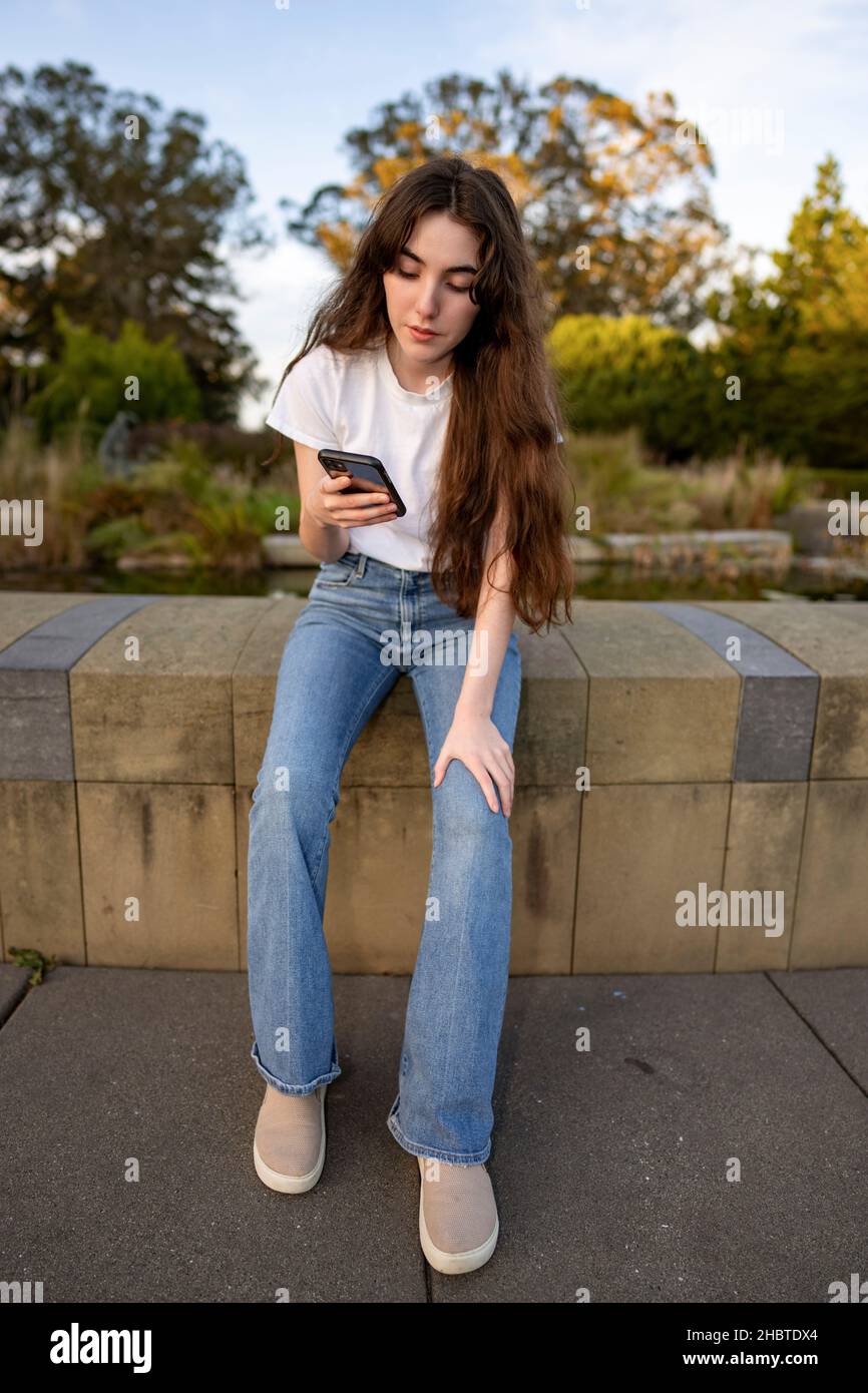 Teenager-Frau, die ihr Smartphone an einem mit Lilly gefüllten Teich benutzt Stockfoto