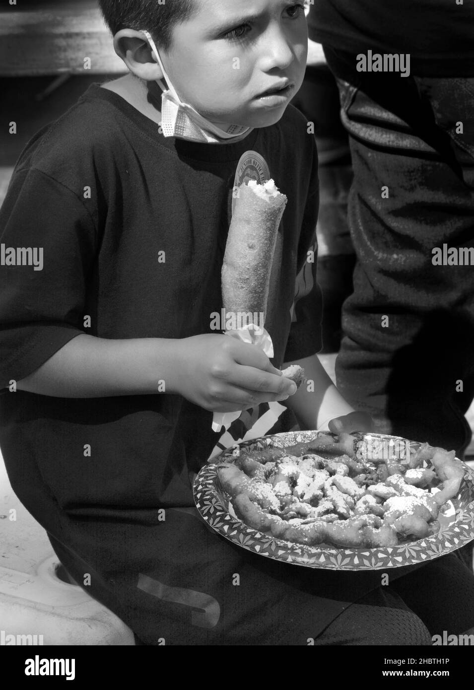 Ein Junge isst auf einem Festival in Santa Fe, New Mexico, einen Trichterkuchen und Hot Dog-on-a-Stick. Stockfoto