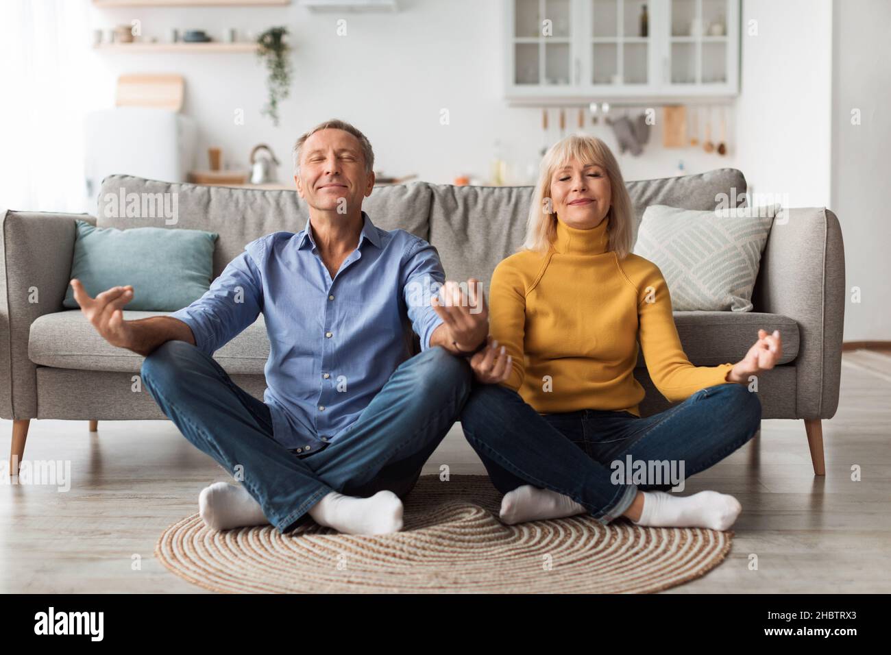 Ältere Ehegatten Meditieren Mit Geschlossenen Augen Und Machen Yoga Zu Hause Stockfoto