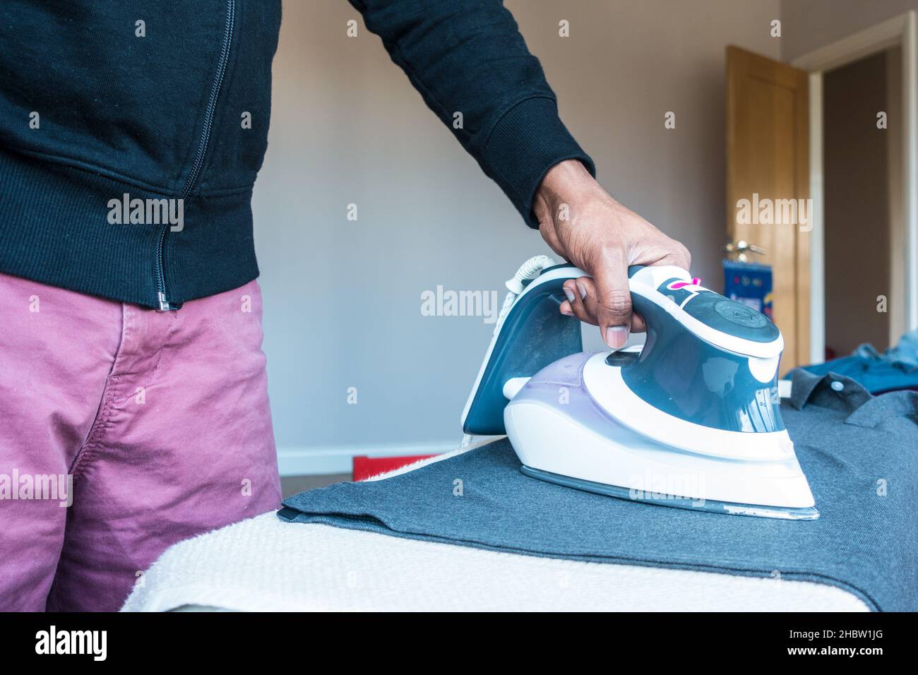 Erwachsene mittelalter indischer Mann presst Poloshirt-Kleidung auf einem Iron Borad Stand Stockfoto