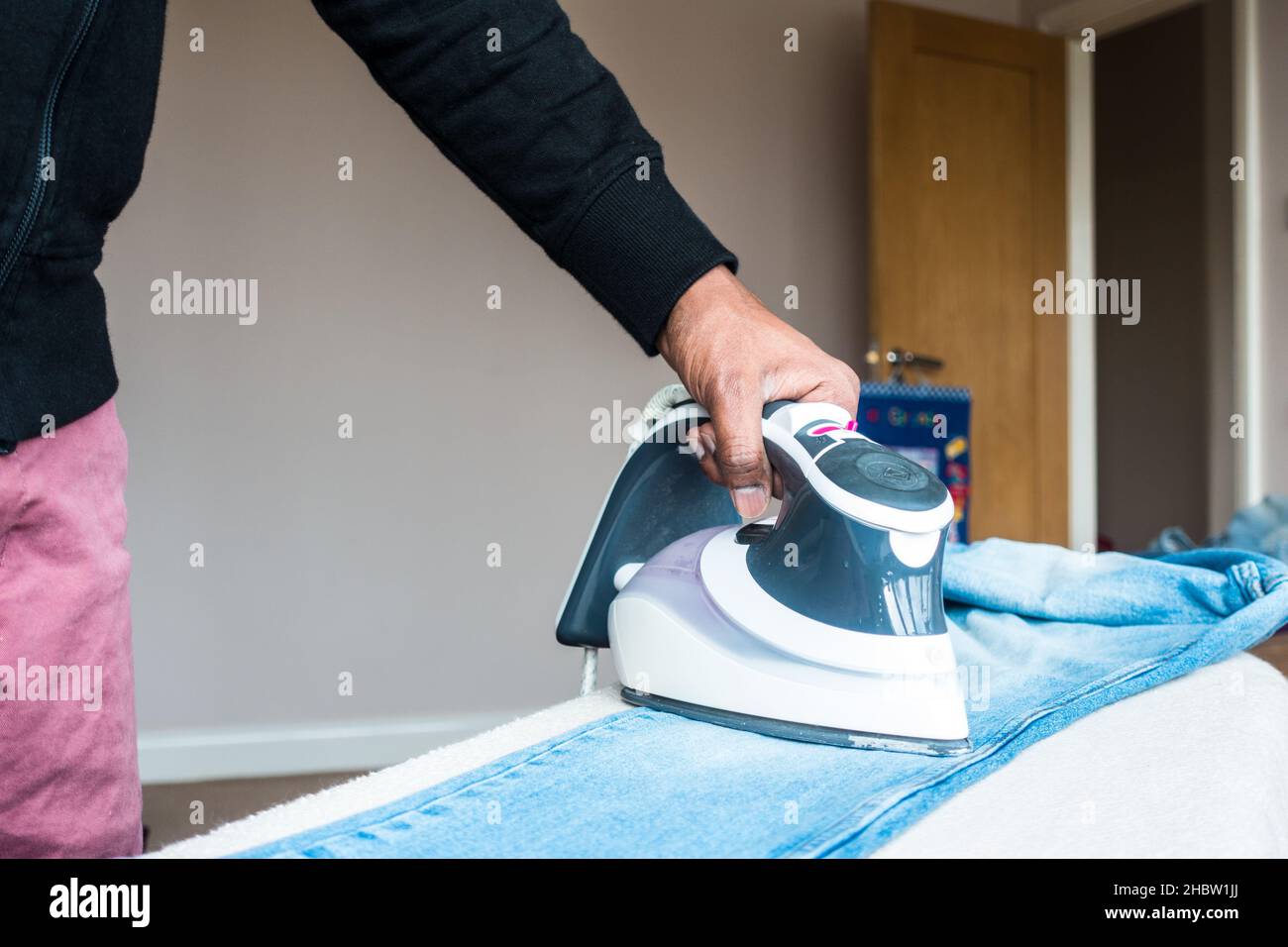 Indischer Mann mittleren Alters drückt Jeans-Hosen auf einem Iron Board Stand Stockfoto