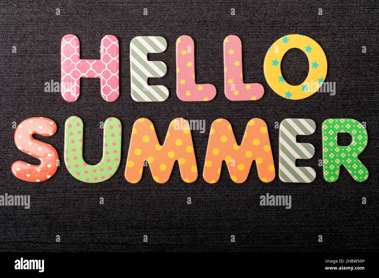 Karte mit „Hello Summer“-Wörtern aus bunt gemischten Holzbuchstaben auf einem strukturierten dunkelschwarzen Textilmaterial, das als Botschaft verwendet werden kann Stockfoto