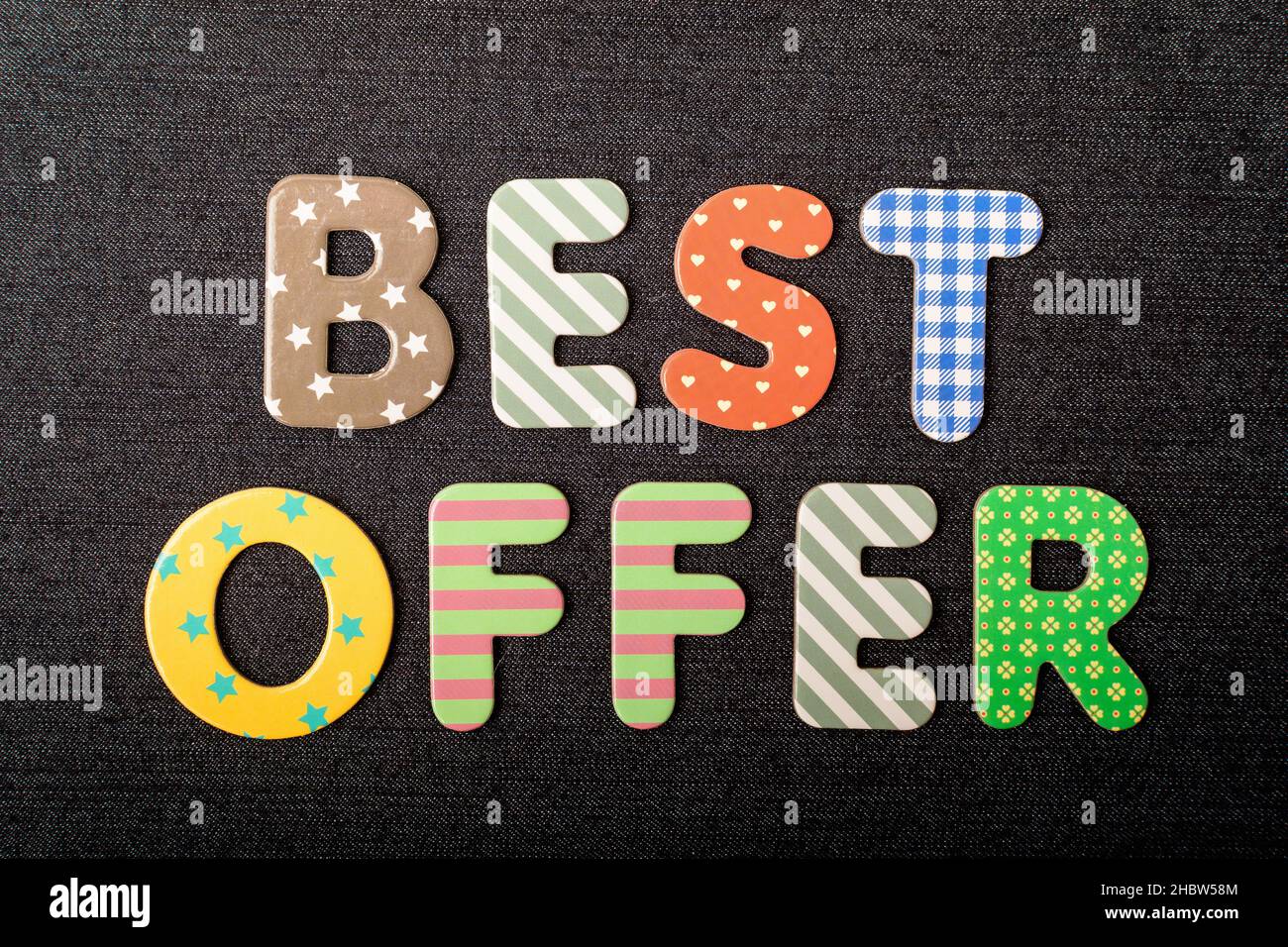 Karte mit Best Offer Wörtern aus gemischten, lebendigen farbigen Holzbuchstaben auf einem strukturierten, dunkelschwarzen Textilmaterial, das als Botschaft verwendet werden kann Stockfoto
