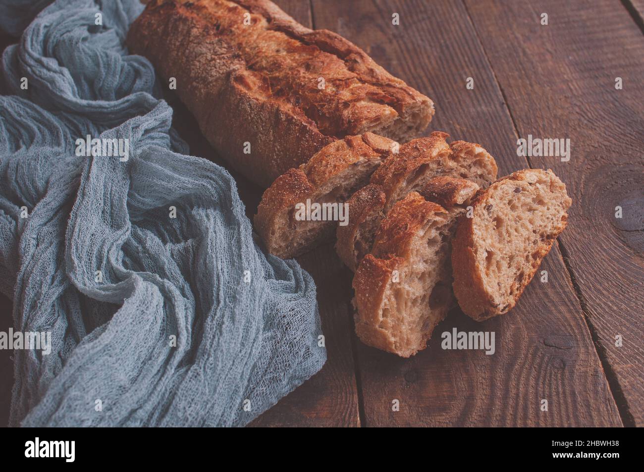 Gebackenes hausgemachtes Brot auf einem Holztisch mit einer grauen Gaze-Tischdecke, frisch geschnittenes Baguette auf einem Holzhintergrund Stockfoto